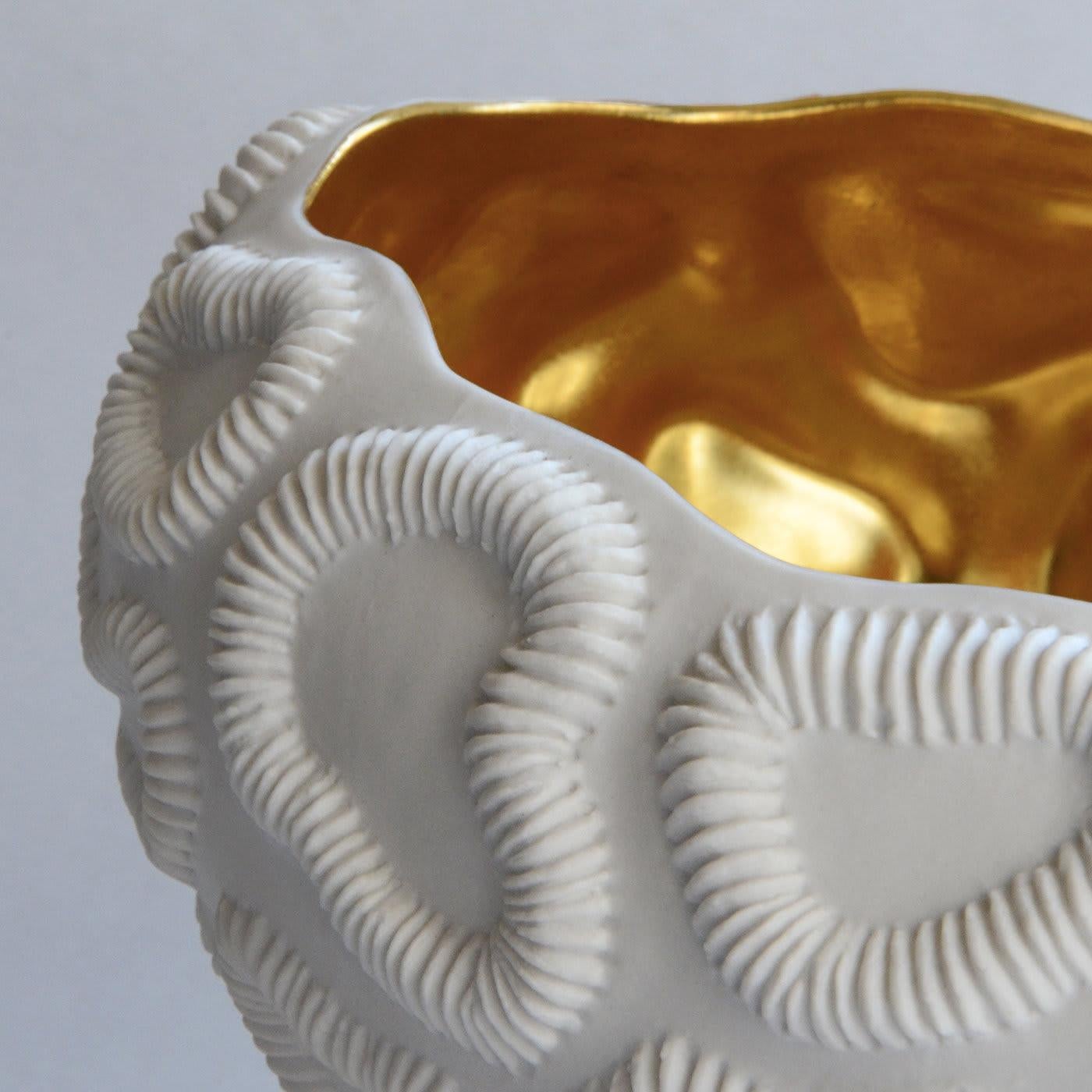 Inspired by madrepore fossils, this exquisite oval-shaped bowl merges traditional craftsmanship with daring modern aesthetic. The shell-white exterior features irregularly shaped, circular motifs with textural ridges, evoking the surface of