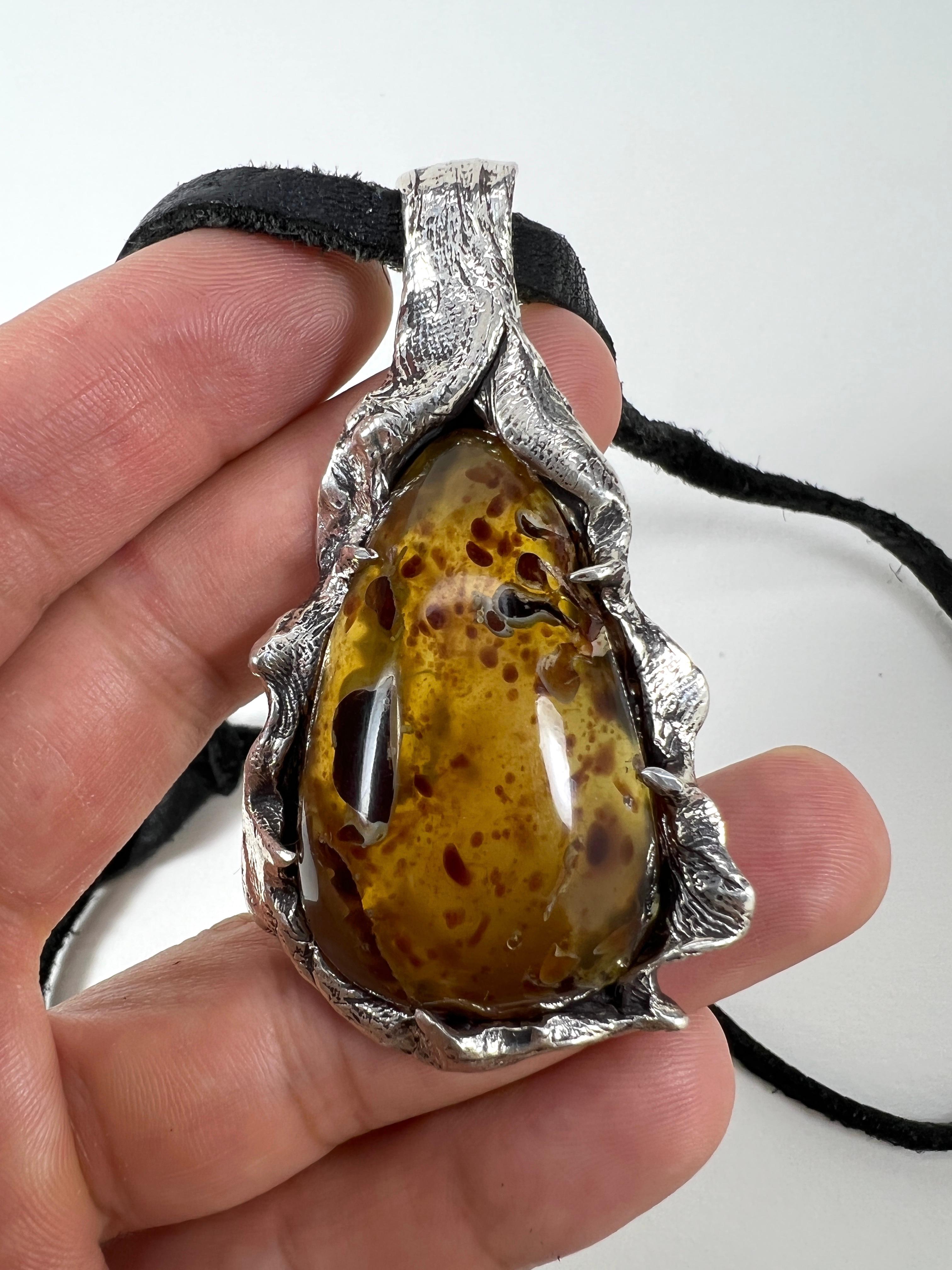Fossilized Paradise is a one-of-a-kind pendant by Ken Fury that is hand-carved and cast in sterling silver and features a natural amber fossil. Look back millions of years in history as you look into the amber, for it takes that long to fossilize.