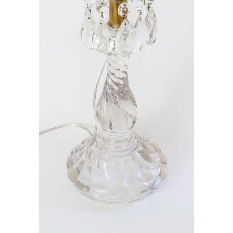 Glass candlestick lamp, made by Fostoria in the colony pattern in the mid 20th Century. Swirled pressed glass base, with a brass top, glass bobeche and crystals. Includes new white paper shade, 16 x 10 x 11. In good condition, one chip at the top of