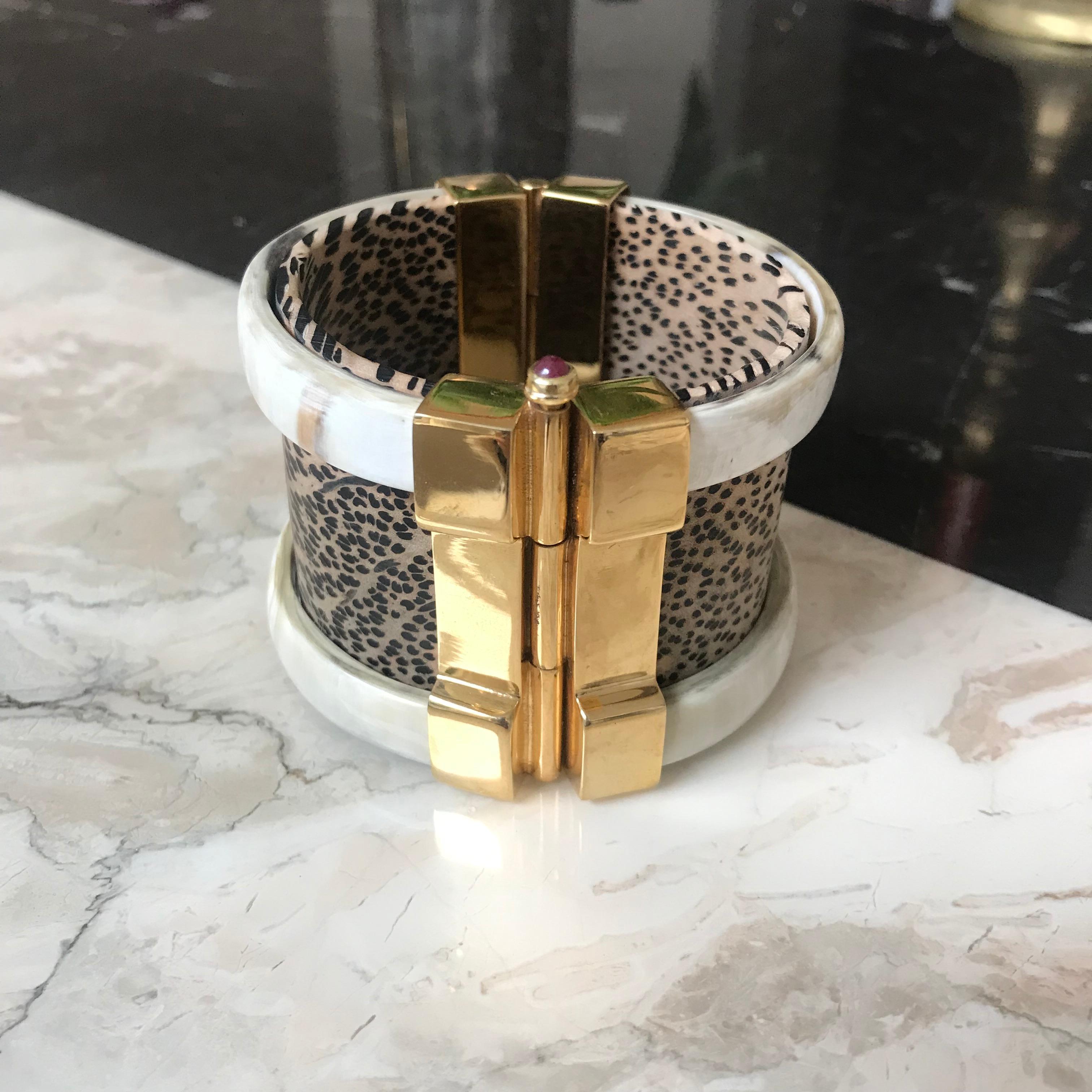 Cuff bracelet crafted from African wood and cow horn. The customizable 18k gold plate pin-clasp is set with a choice or ruby or emerald. Inspired by warrior style cuffs worn by Diana Vreeland. 

This is a bespoke piece with a lead time of 2-3