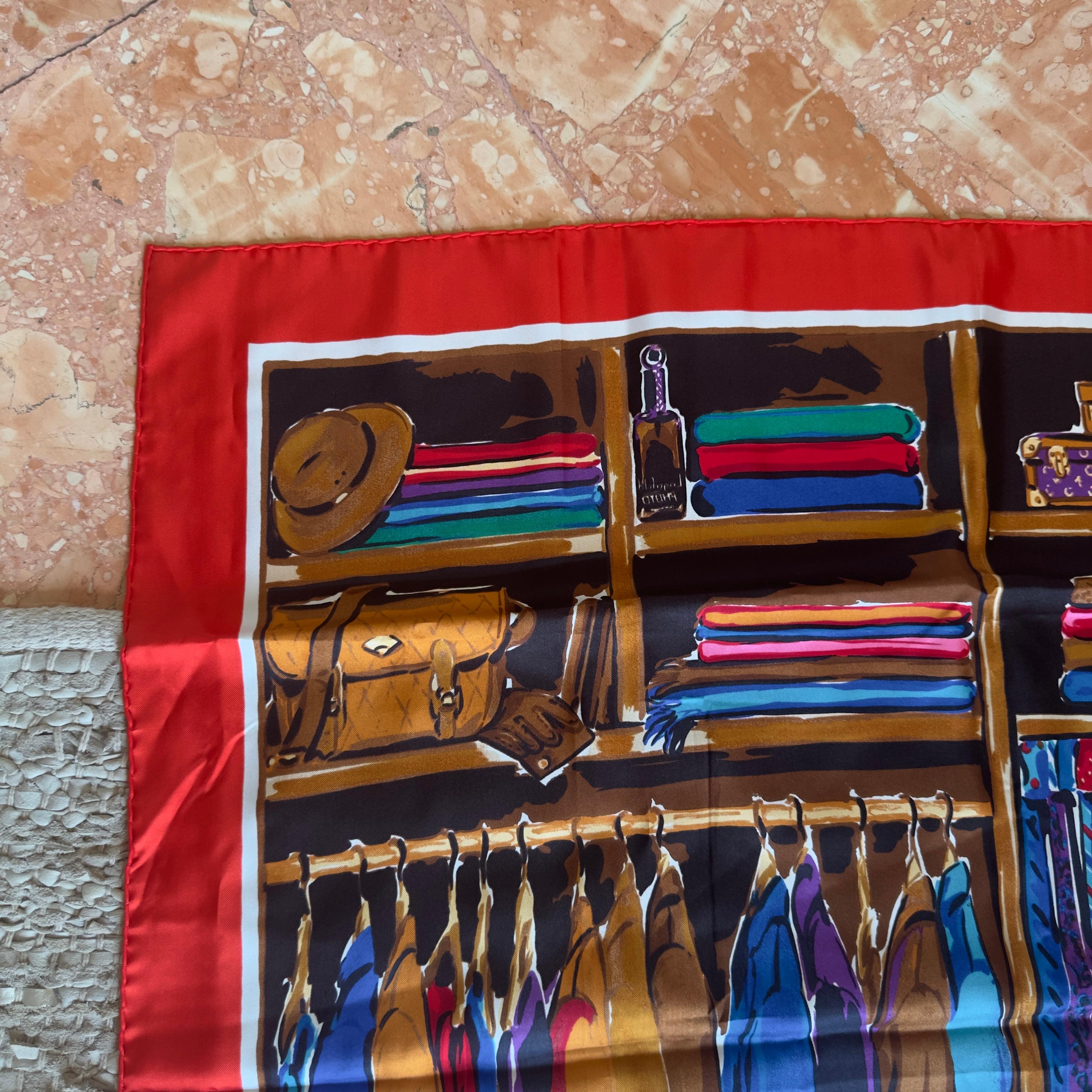 Un icónico pañuelo de Karl Lagerfeld, confeccionado en pura seda brillante con un borde rojo y un llamativo estampado que representa un elegante vestuario masculino completo con abrigos, corbatas, zapatos y accesorios. Una pieza rara e irónica que