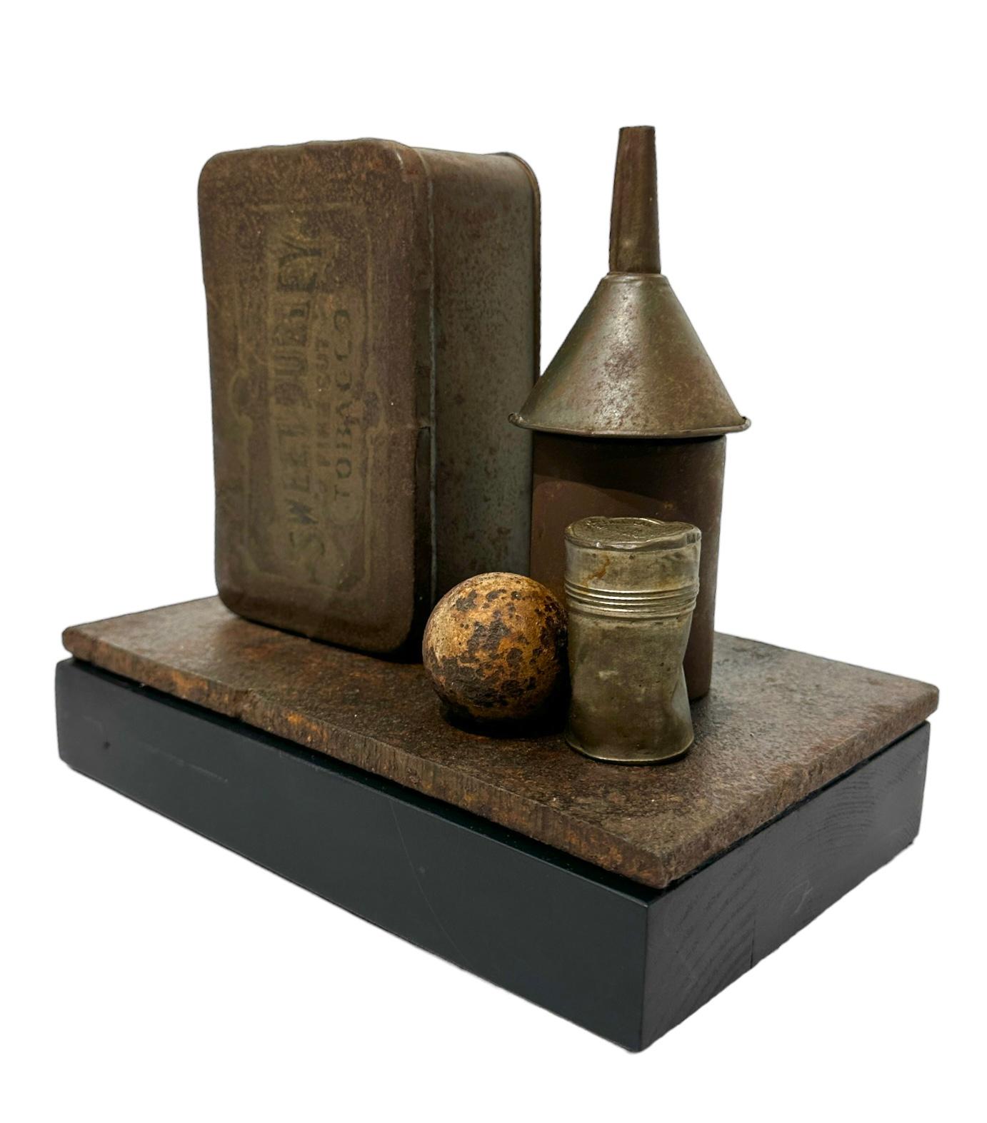 Jim Rose, known primarily for his steel furniture, was an avid collector and scoured salvage yards for unique, interesting items.  Here, a beautifully rusted tobacco box, a steel egg, a funnel and two small canisters are mounted to a steel base,