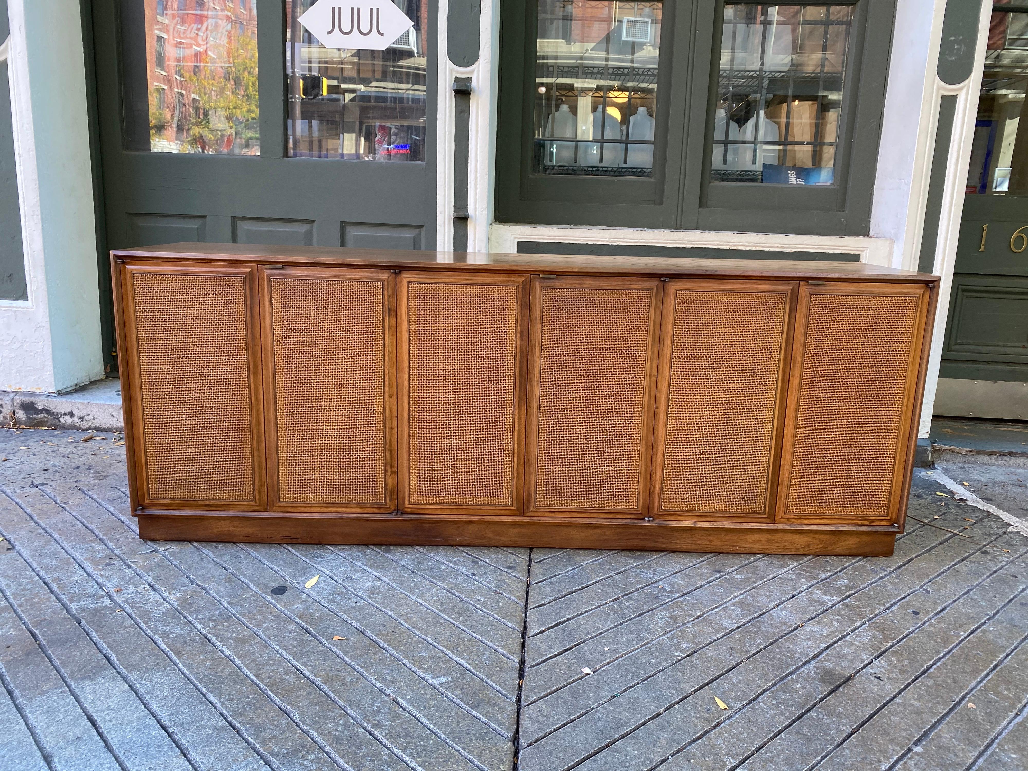 Founders 6-door caned front credenza/ buffet. Walnut finish, with 3 sets of double doors. Each door opens to reveal an adjustable shelf and 1 pull out. Very nice clean condition! Nice simple lines that go with any interior!