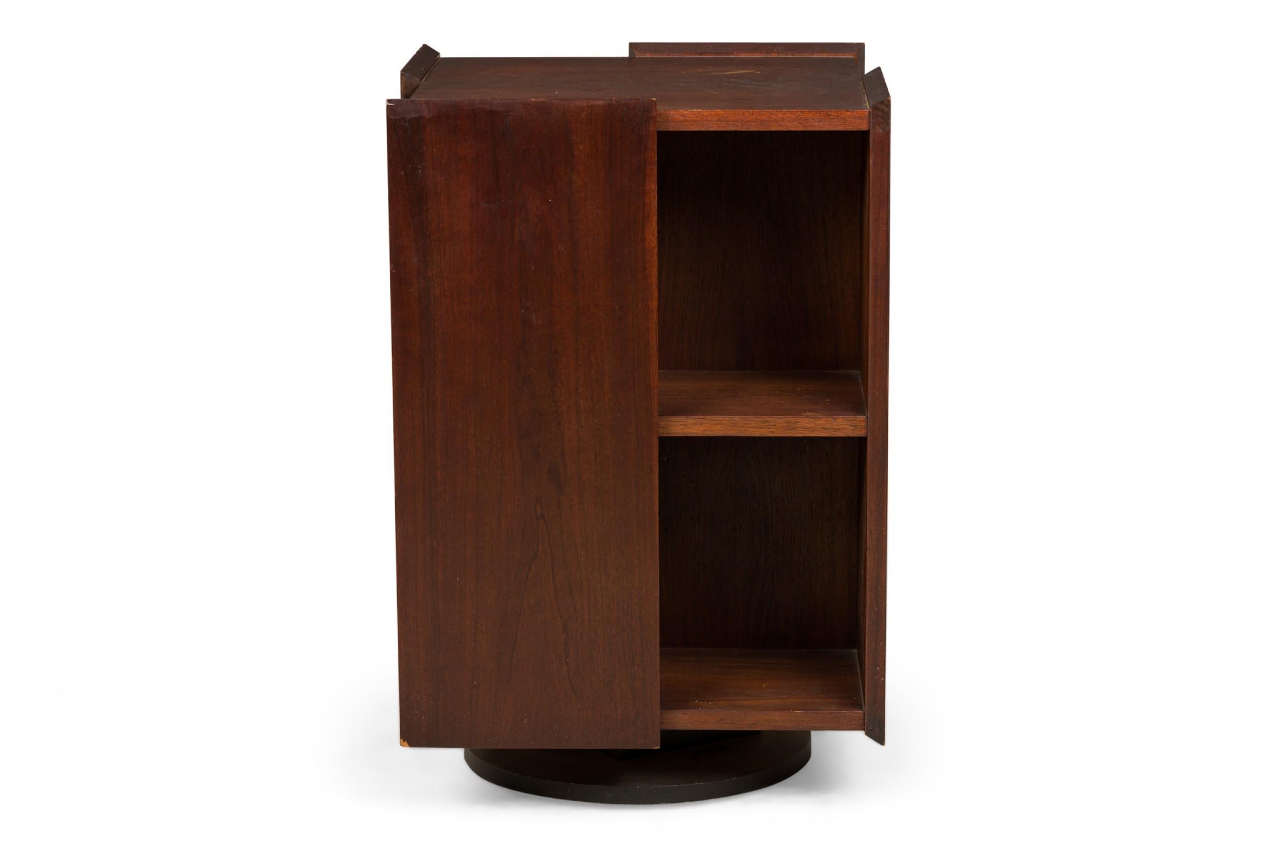 American mid-century dark walnut lazy susan mini-bookcase with a rectangular form of alternating panels and two compartment shelves on each side, on a fully rotational plinth base. (FOUNDERS)