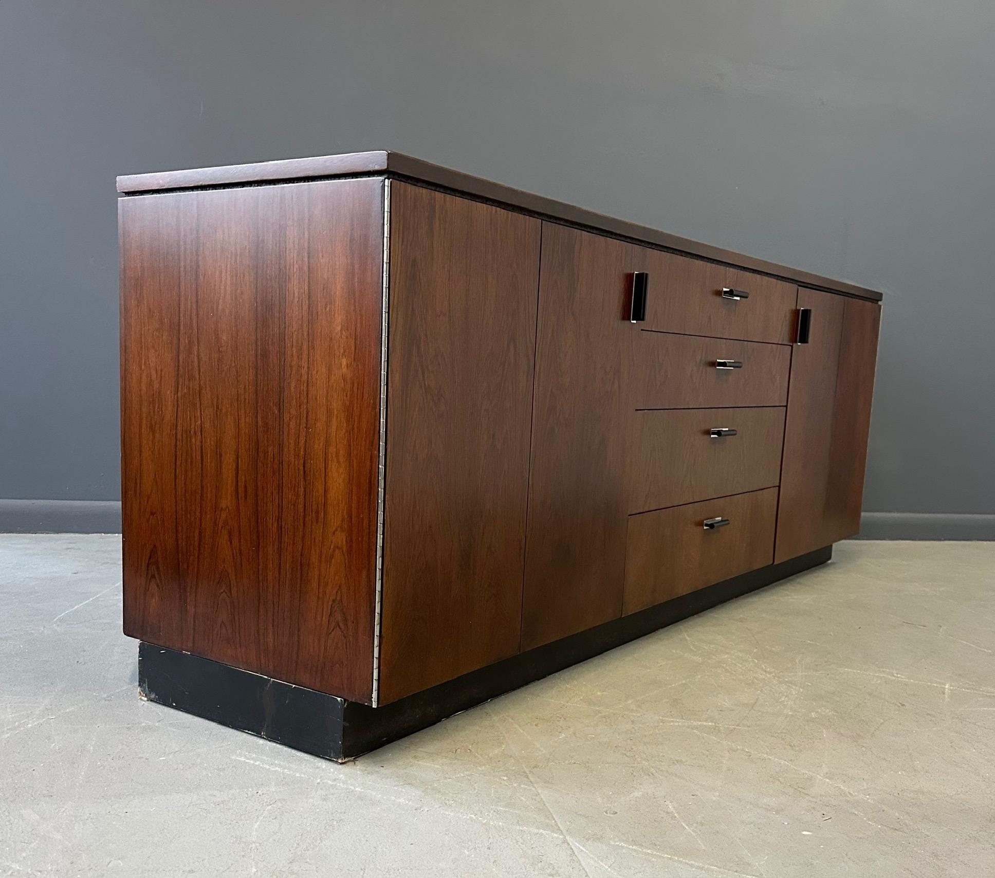 Questa credenza in legno di palissandro di Founders offre un ampio spazio di archiviazione grazie ai suoi cassetti e ai suoi ripiani, che la rendono un'aggiunta pratica ed elegante a qualsiasi casa. Realizzato con un'impiallacciatura di palissandro