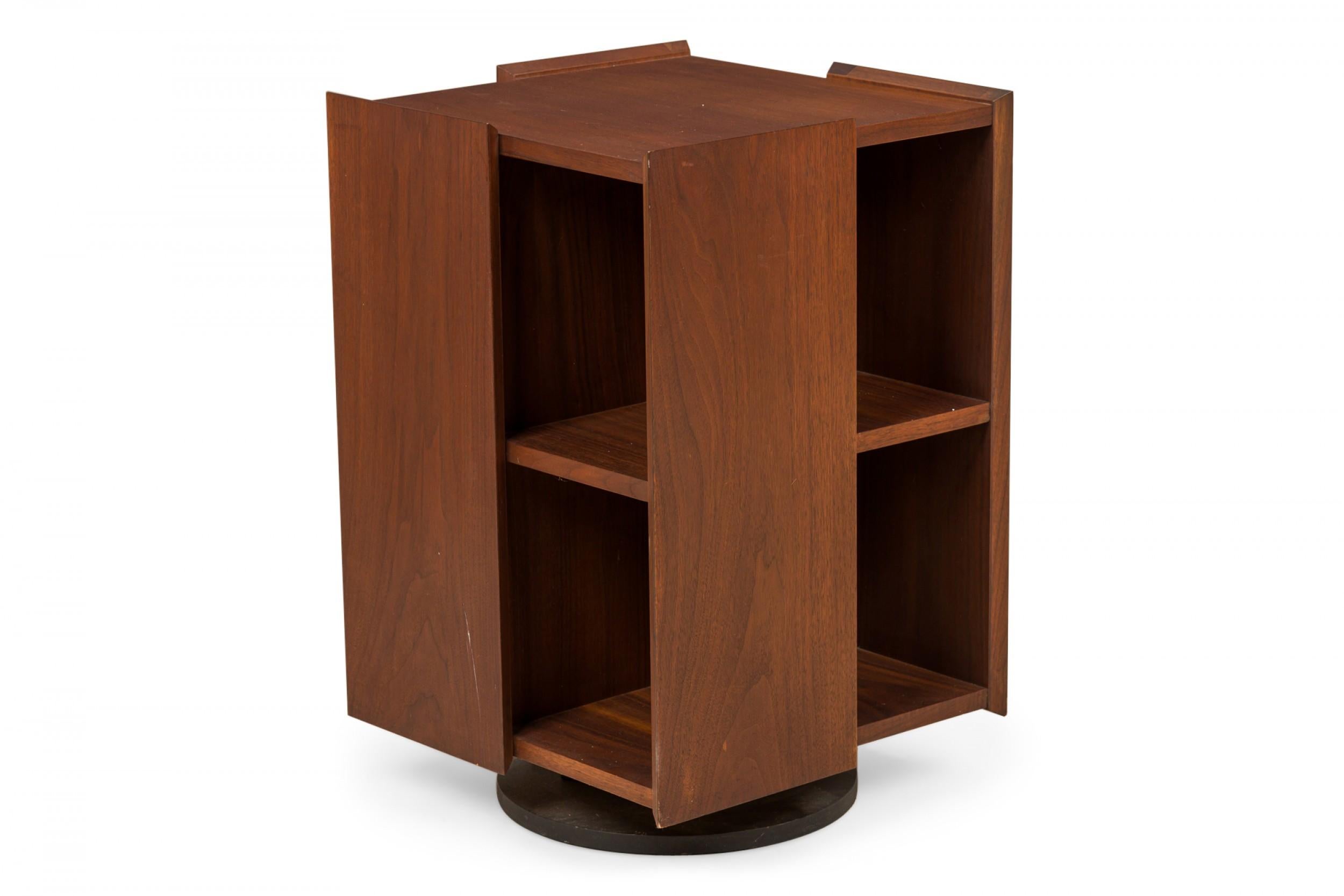 American mid-century walnut lazy susan mini-bookcase with a rectangular form of alternating panels and two compartment shelves on each side, on a fully rotational plinth base. (FOUNDERS)