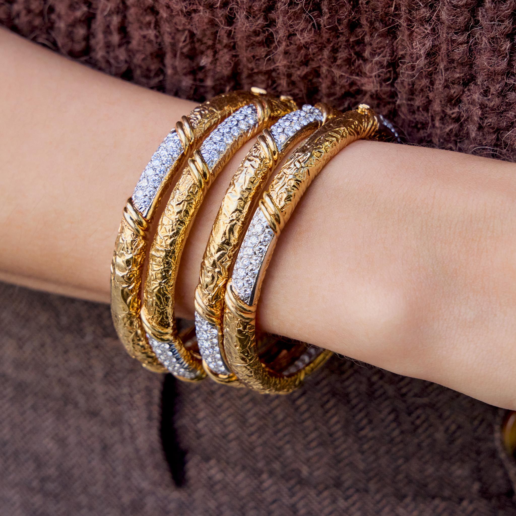 Created by Van Cleef & Arpels, Paris, this set of four 18K gold and diamond bangle bracelets dates from circa 1970. Each hinged bombé form is set with three fields of pavé-set round brilliant-cut diamonds edged by double arch motifs, and alternating