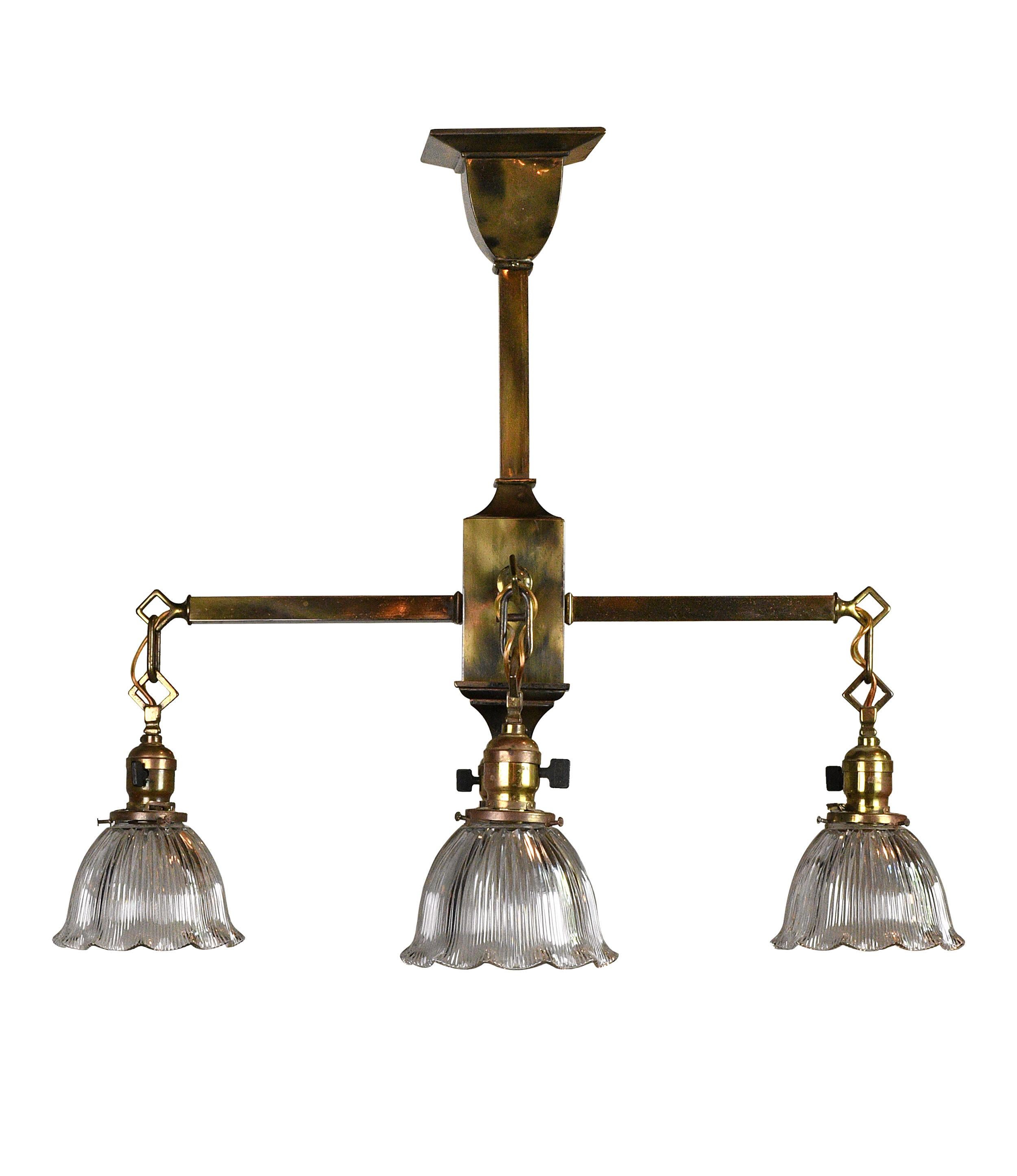 Four-arm brass mission chandelier with four skirted Holophane shades. The brass has a lovely mottled quality that is at once bright and moody, and the scalloped shades add a pleasant sense of movement to the otherwise straight edged fixture.