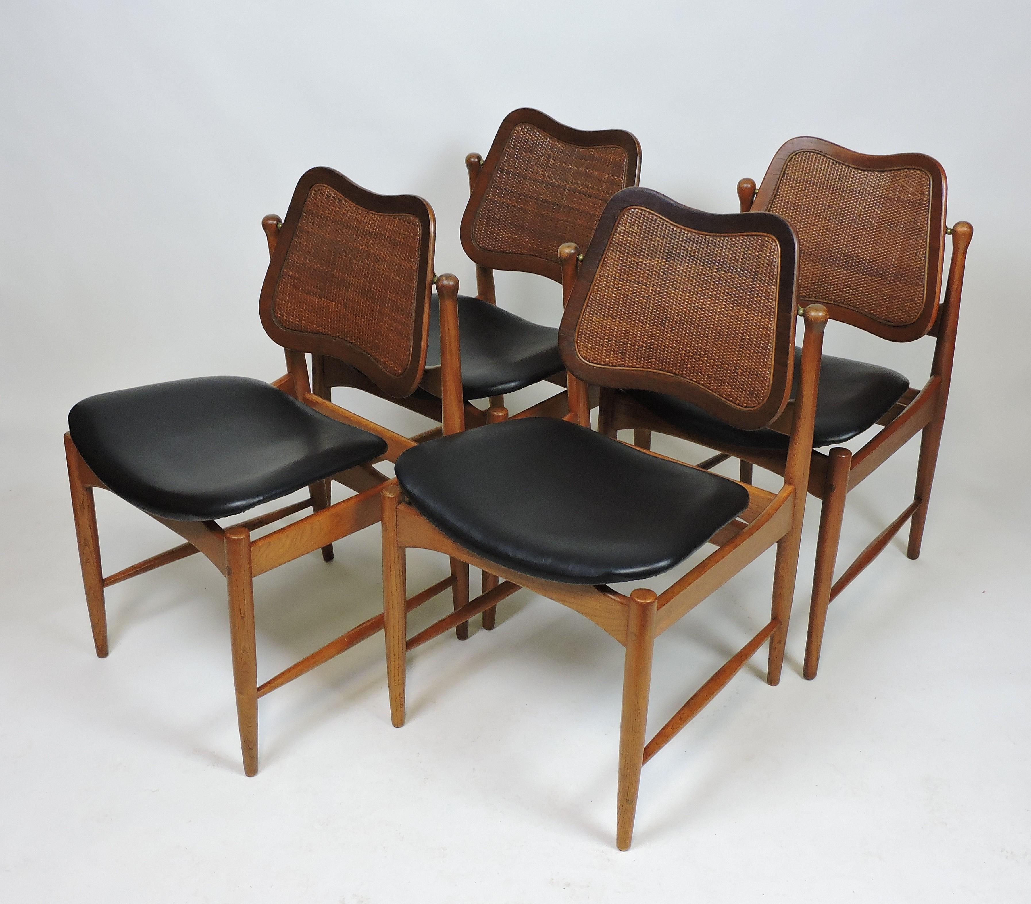 Set of four dining chairs designed by Arne Vodder. These beautiful chairs have floating seats covered in black naugahyde and backs inset with cane that pivot on brass fittings for comfort.