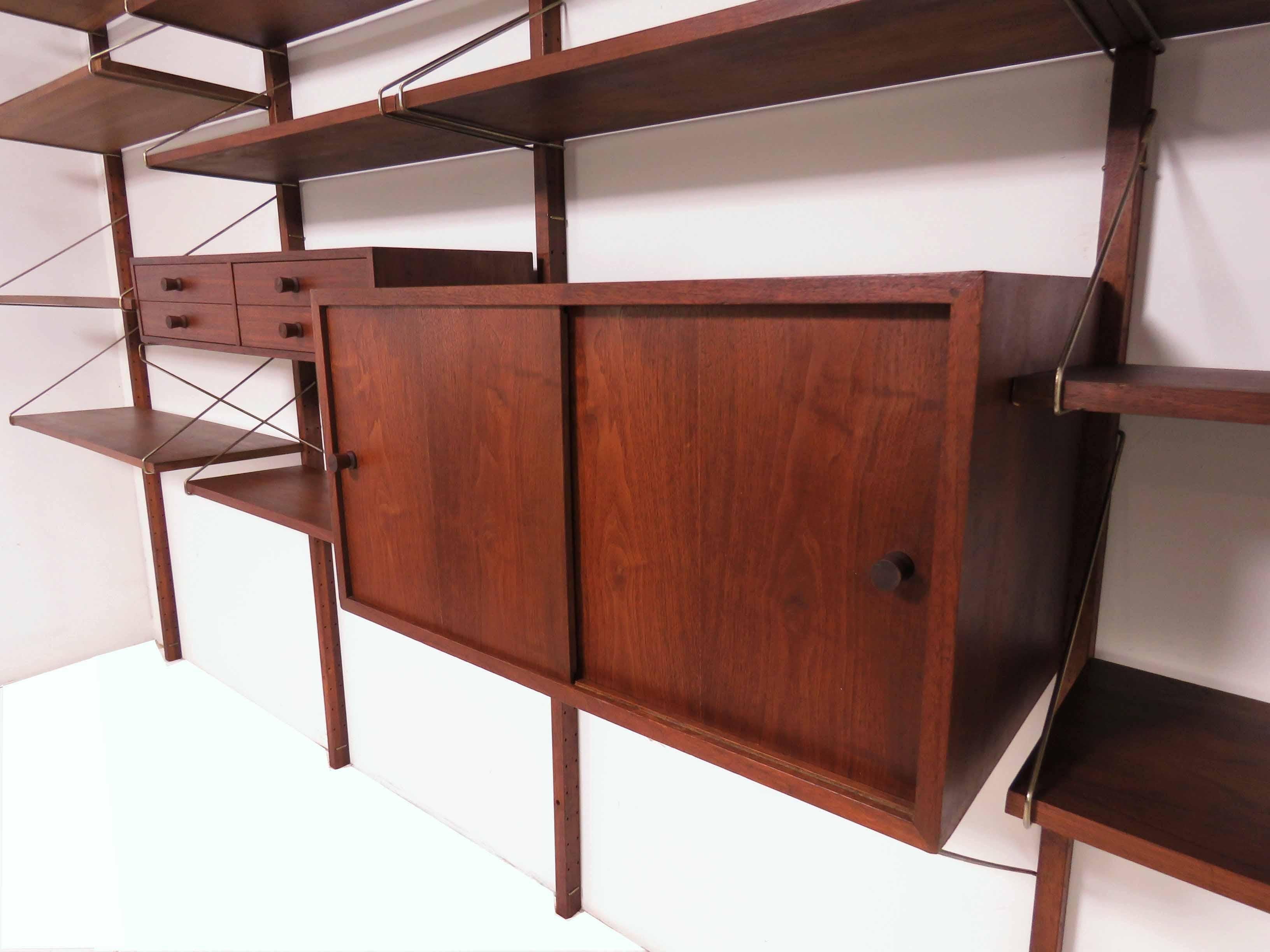 Midcentury wall-mounted shelving unit in walnut, circa 1960s. Four bay unit consists of a cabinet, drawer space and shelving. 

Overall, the wall unit measures 127