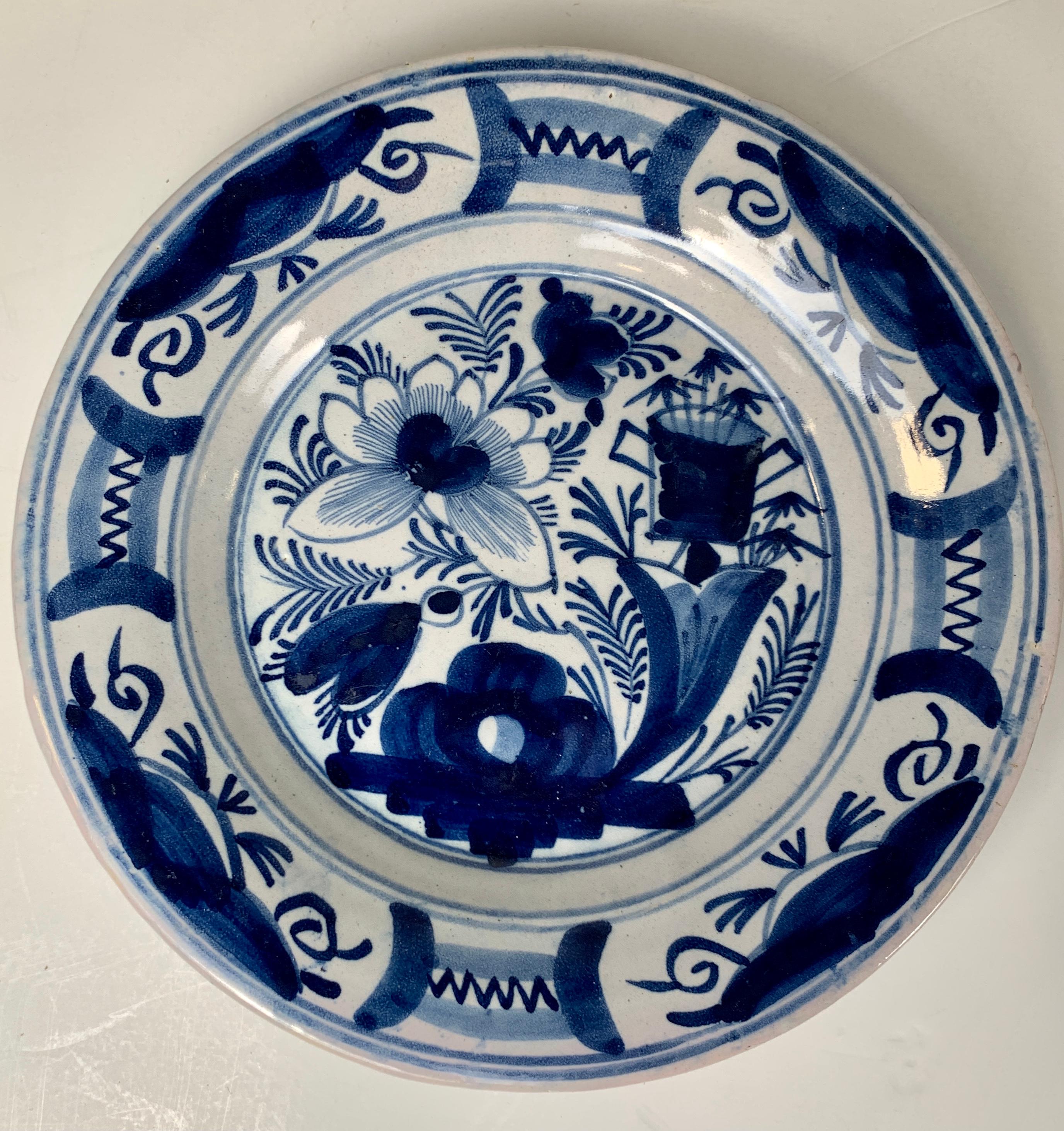 A set of four antique blue and white Dutch Delft dishes showing flowers, a vase, and a pieced rock.
The deep cobalt blue is splendid on the bright white tin glaze background.
The border is filled with four panels each with a floral design. Between