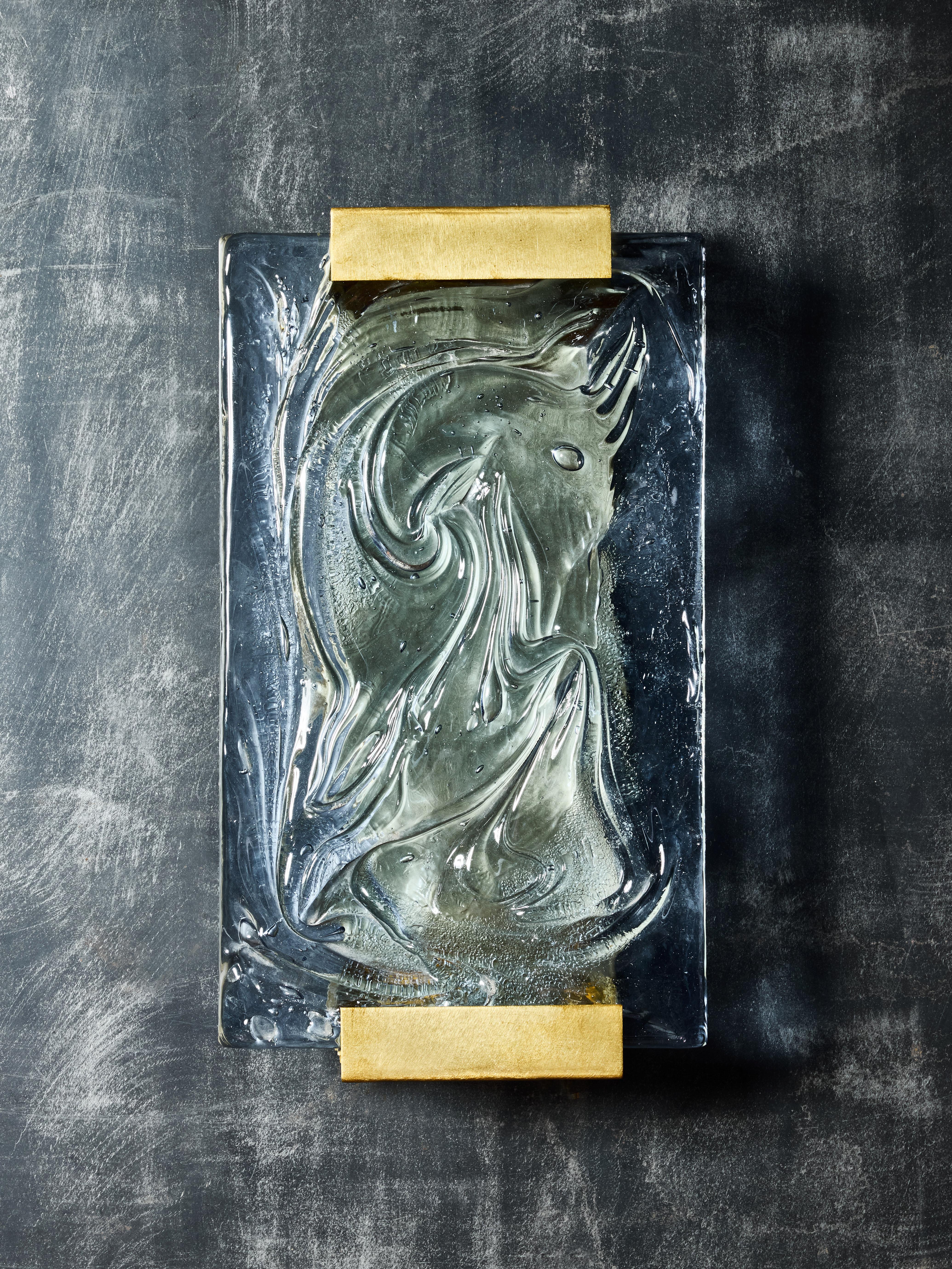 Quatre appliques murales fabriquées à partir de plaques de verre bleu vintage provenant du sud de la France, présentant des vagues et d'autres motifs complexes, élégamment montées sur une monture contemporaine en laiton.
Chaque plaque de verre est