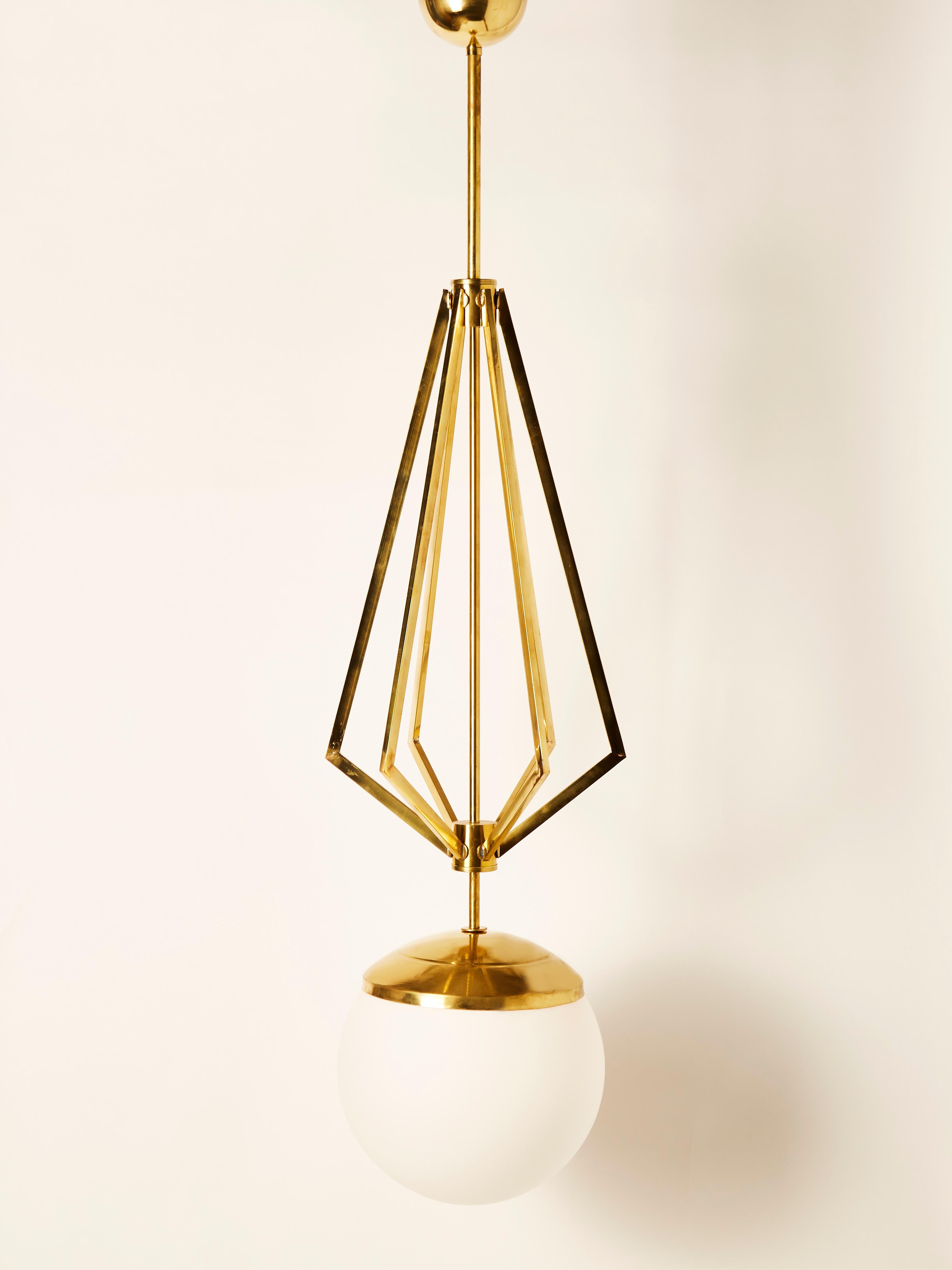 Four suspensions made of a central brass stem, decorative symmetrical rods and a large white glass globe housing a single light source.