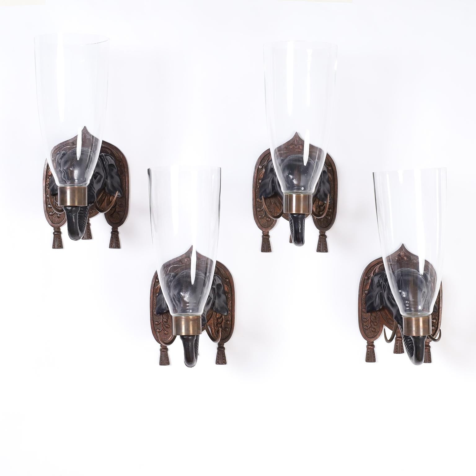 From the San Juan home of iconic American designer Billy Baldwin a set of four antique Italian carved wood wall sconces with carved and ebonized elephant heads, brass tusks, carved back plates, with tassels, and hand blown hurricane shades. Priced