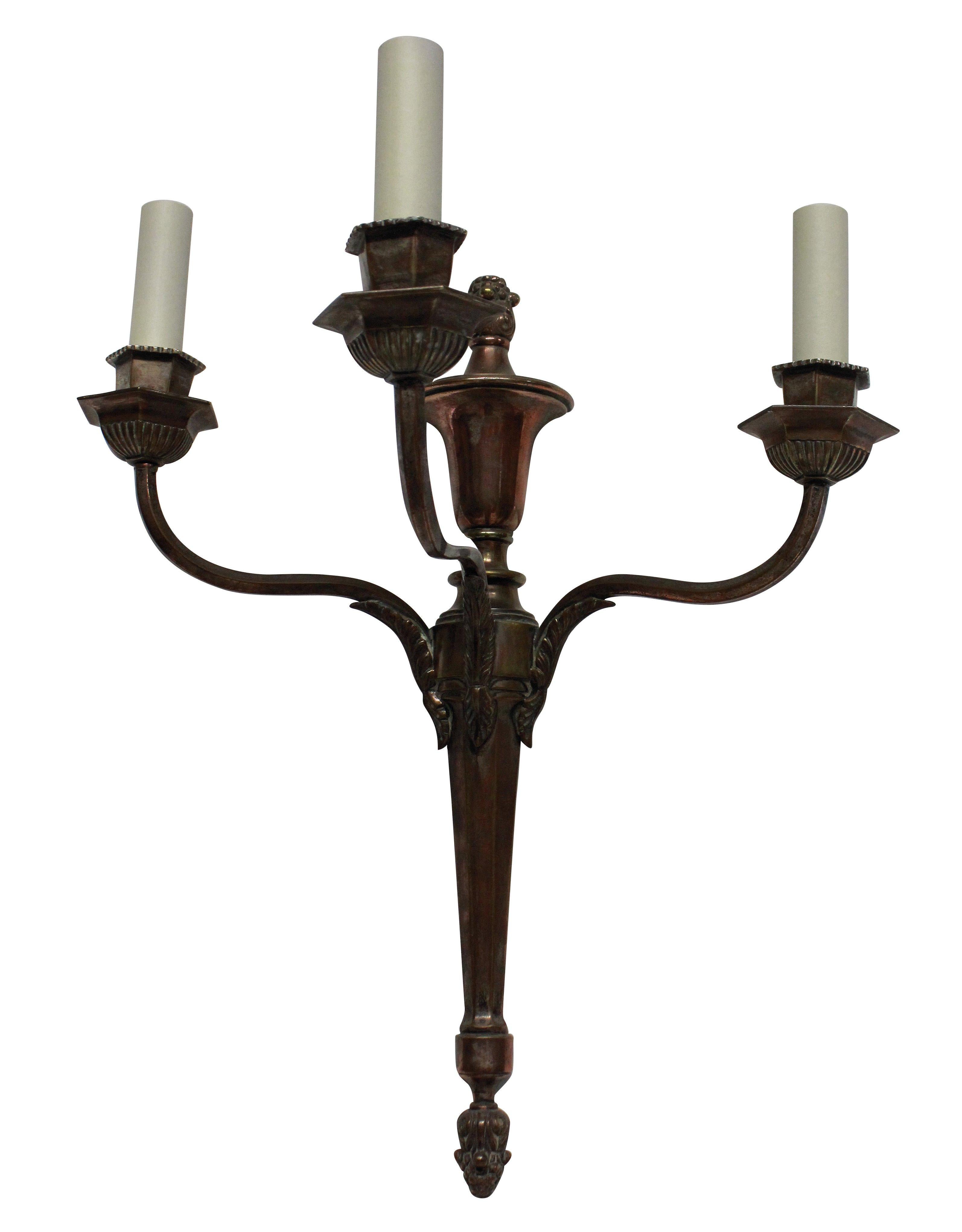 A set of four English neoclassical three-branch wall sconces in an un-restored bronzed finish.