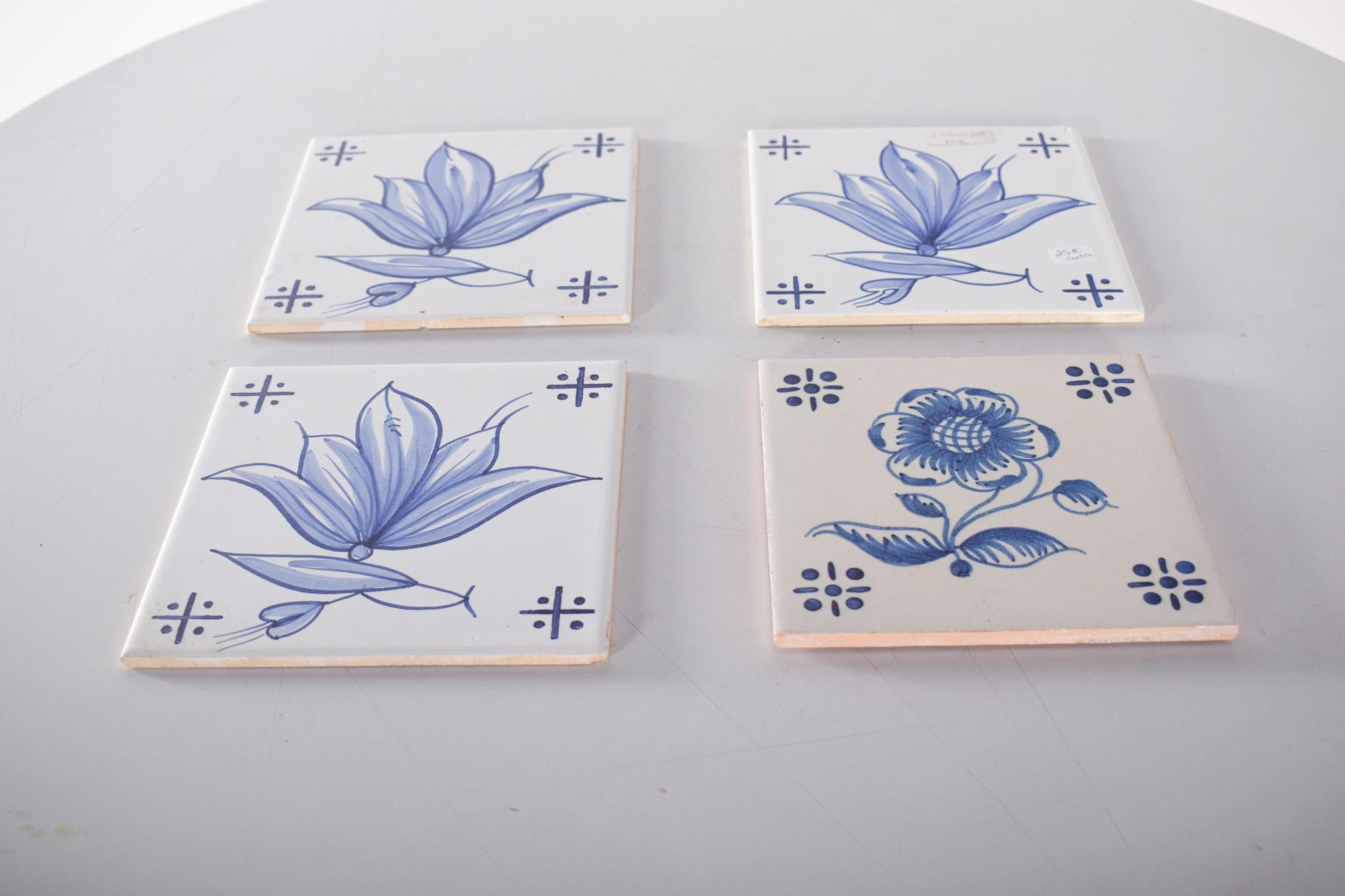 Quattro piastrelle in ceramica, blu e bianche. Decorazione tradizionale portoghese con motivi floreali dipinti a mano nei toni del blu su sfondo bianco. Tre di esse mostrano un fiore di loto stilizzato, con petali delicatamente disegnati e piccoli
