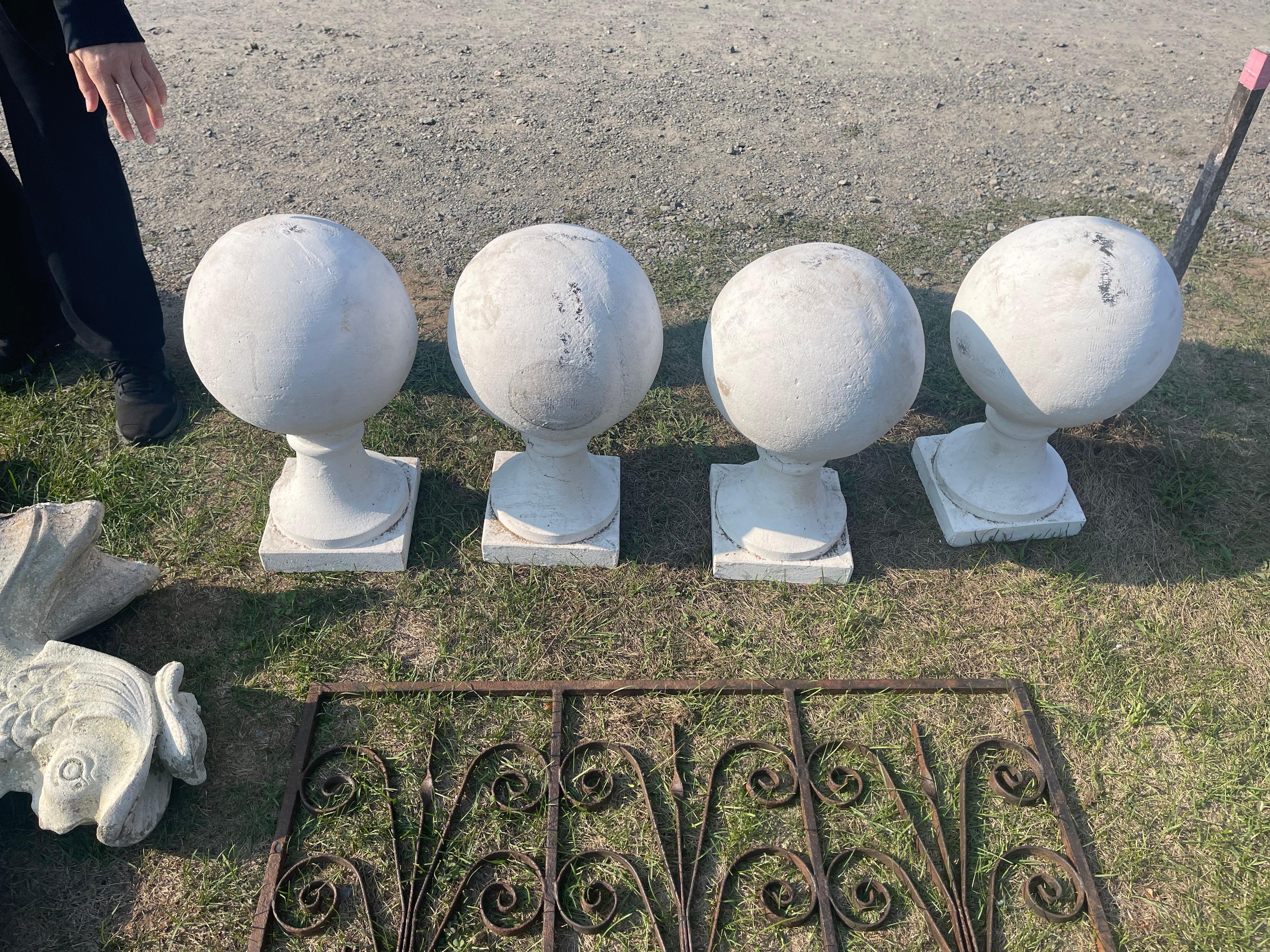 A set of four cement ball finials on pedestal bases painted white from a North Shore estate. The four white-painted finials are stately round balls sitting on elegant tapering pedestals on a 9-inch by 9-inch square base. The ball finials would be
