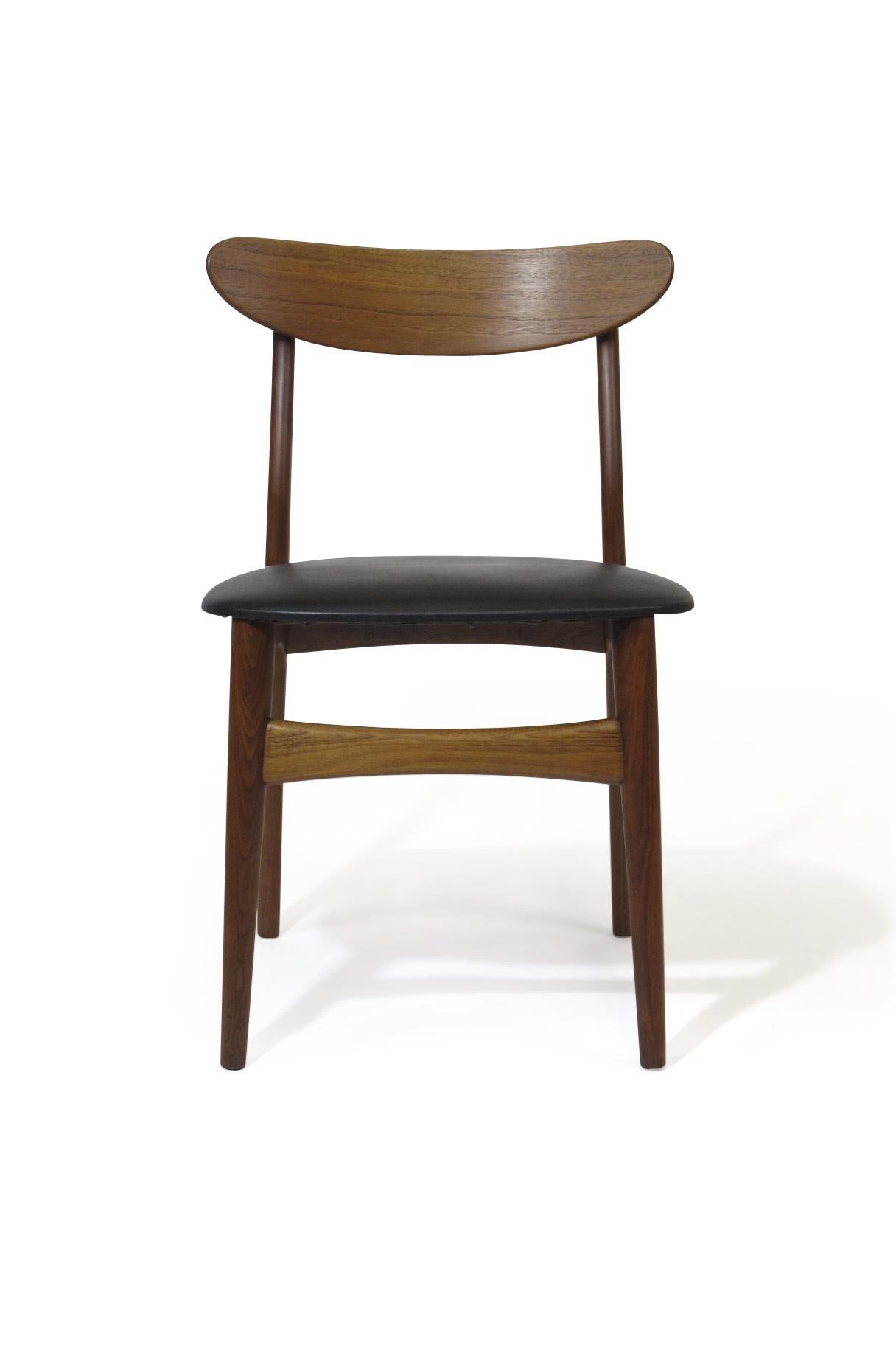 Four Danish midcentury dining chairs crafted of walnut with original black vinyl upholstered seats. Professionally restored and in excellent condition with minor signs of age used. Custom upholstery options available upon request.