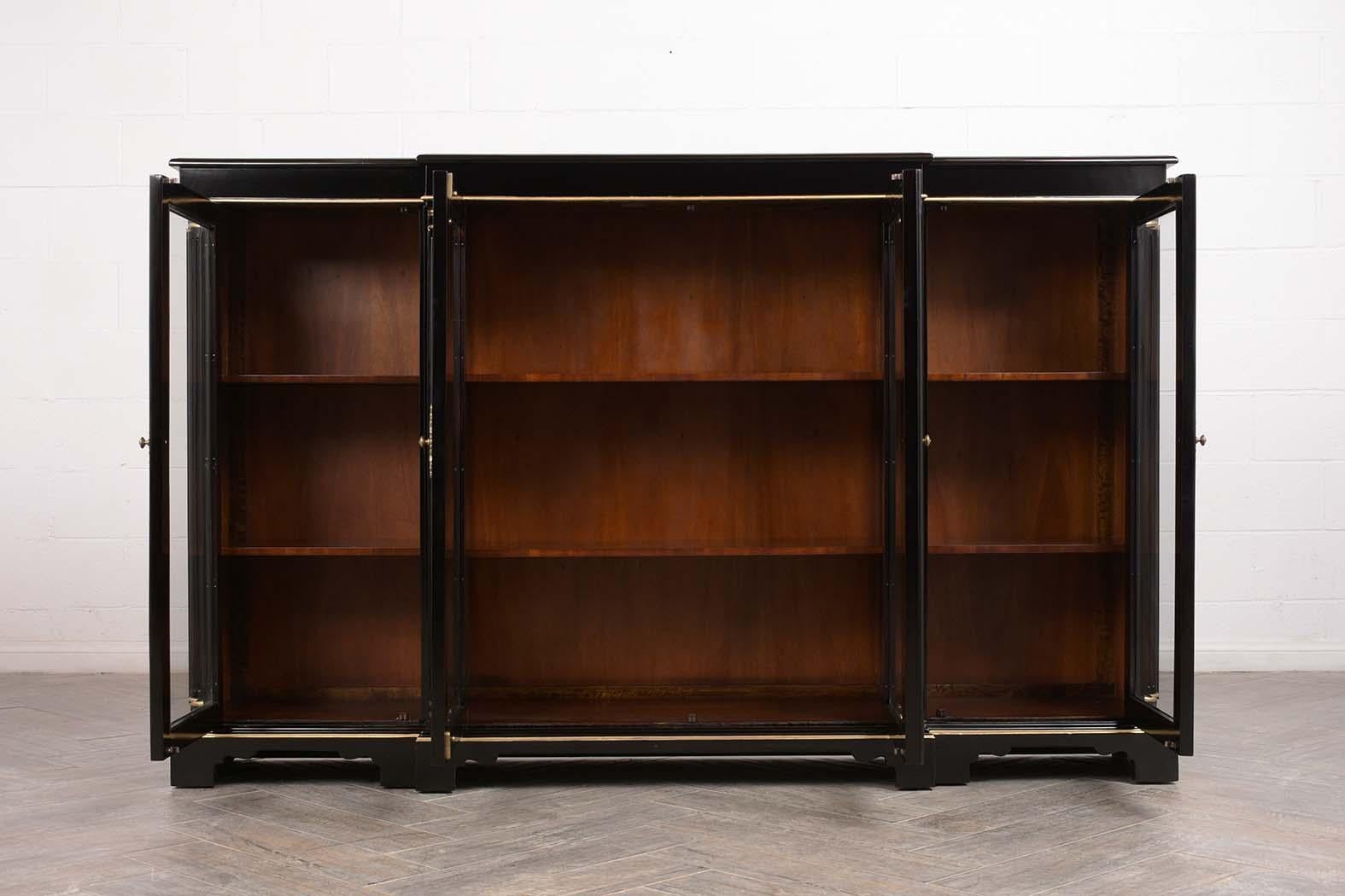 This Regency style mahogany wood four-door bookcase has been restored and finished in a black lacquered color. This bookcase features four doors with original glass, locks and key in working condition, and two interior adjustable wooden shelves. It