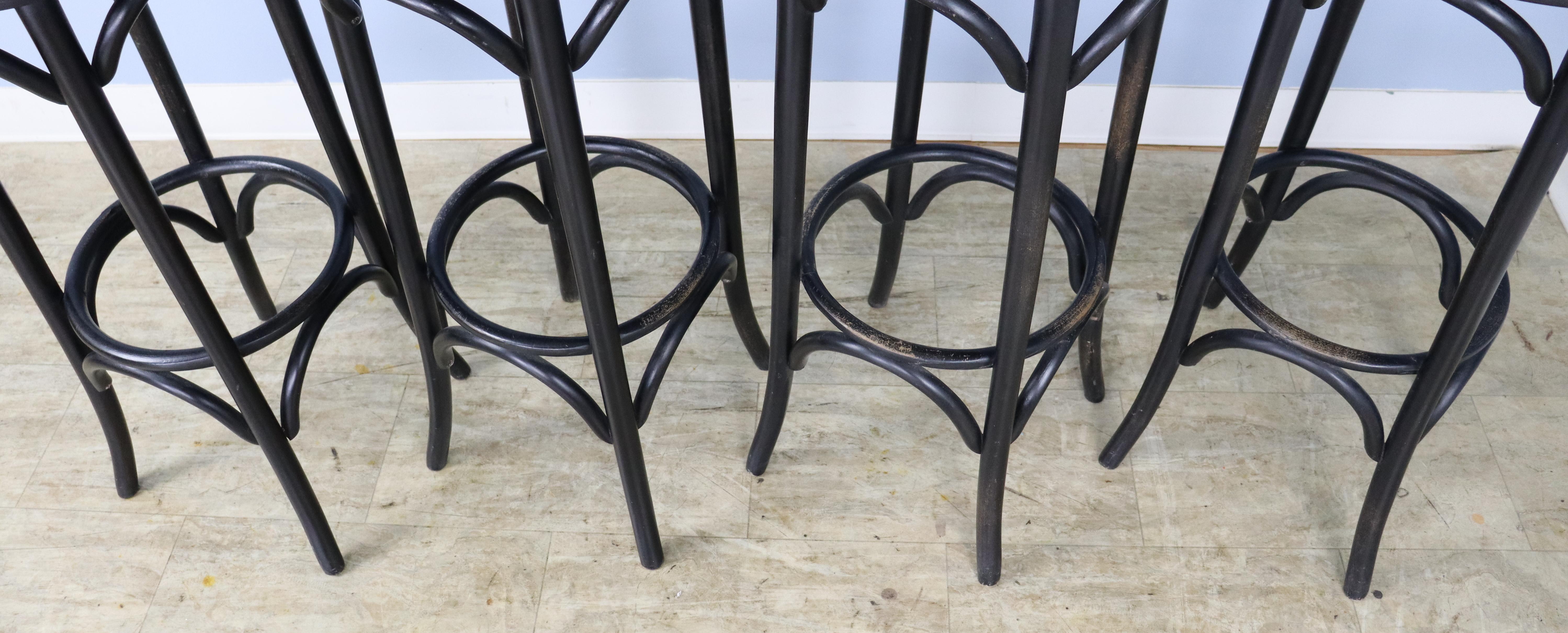 A set of four bent wood bar stools, ebonized and newly upholstered in an oatmeal linen.  The circular foot supports show wear, but we have left them in their original condition.  The stools are sturdy - no wobbles!  A repair has been made to one of