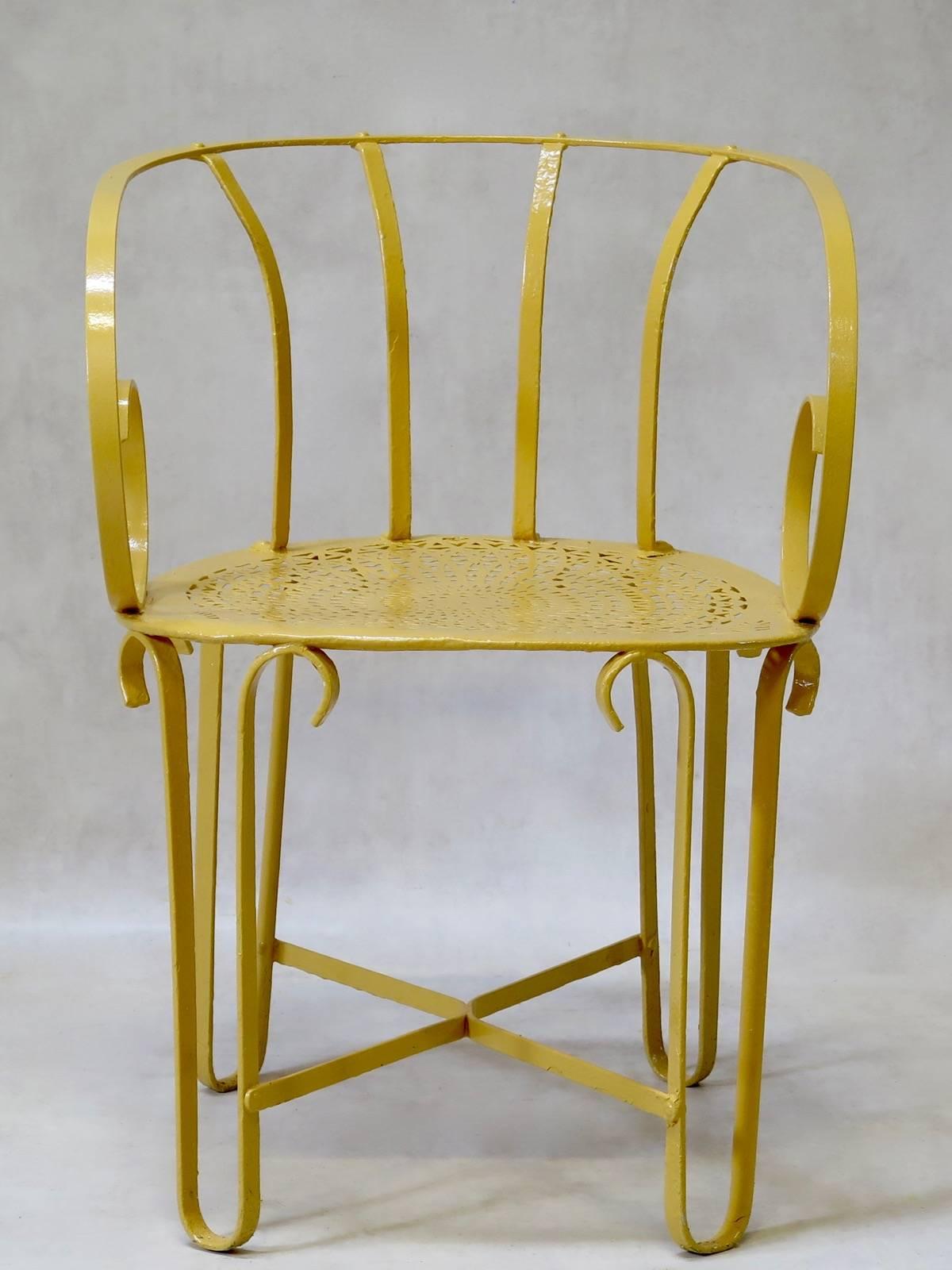 Unusual set of four wrought-iron armchairs, painted yellow. The chairs have rounded, barrel backs and scrolled armrests. The are riveted onto the bases, the large seats of which have a delicate, cutout pattern. The legs are joined by an X-shape