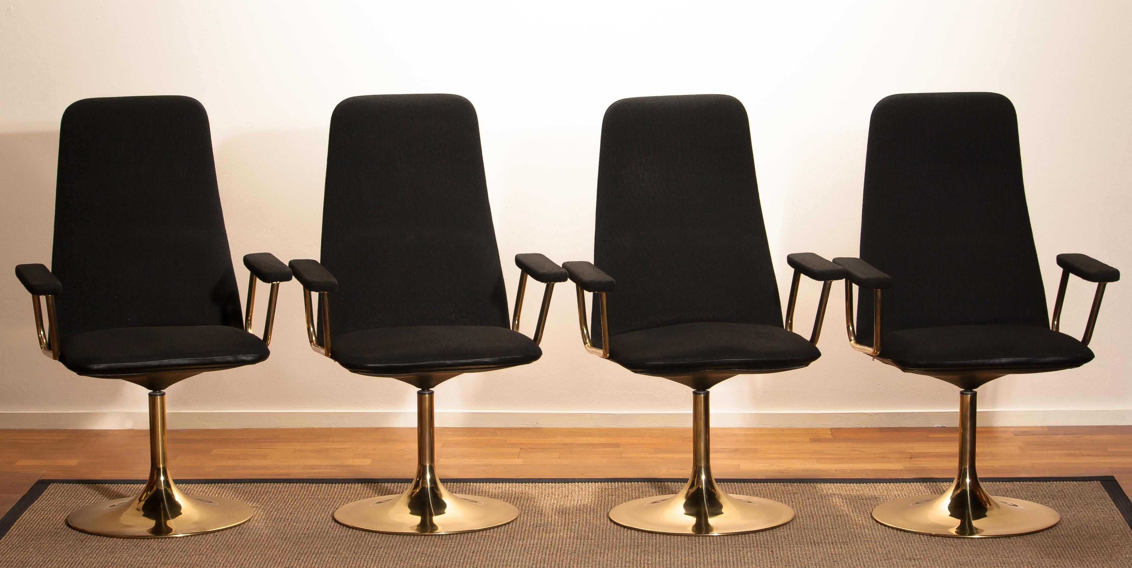 Set of four early production golden swivel chairs with arm rests by Börje Johanson Design for Markaryd Sweden. 
Upholstered with black fabric and a black faux leather back on golden steel bases.
The chairs are in a good condition and from the