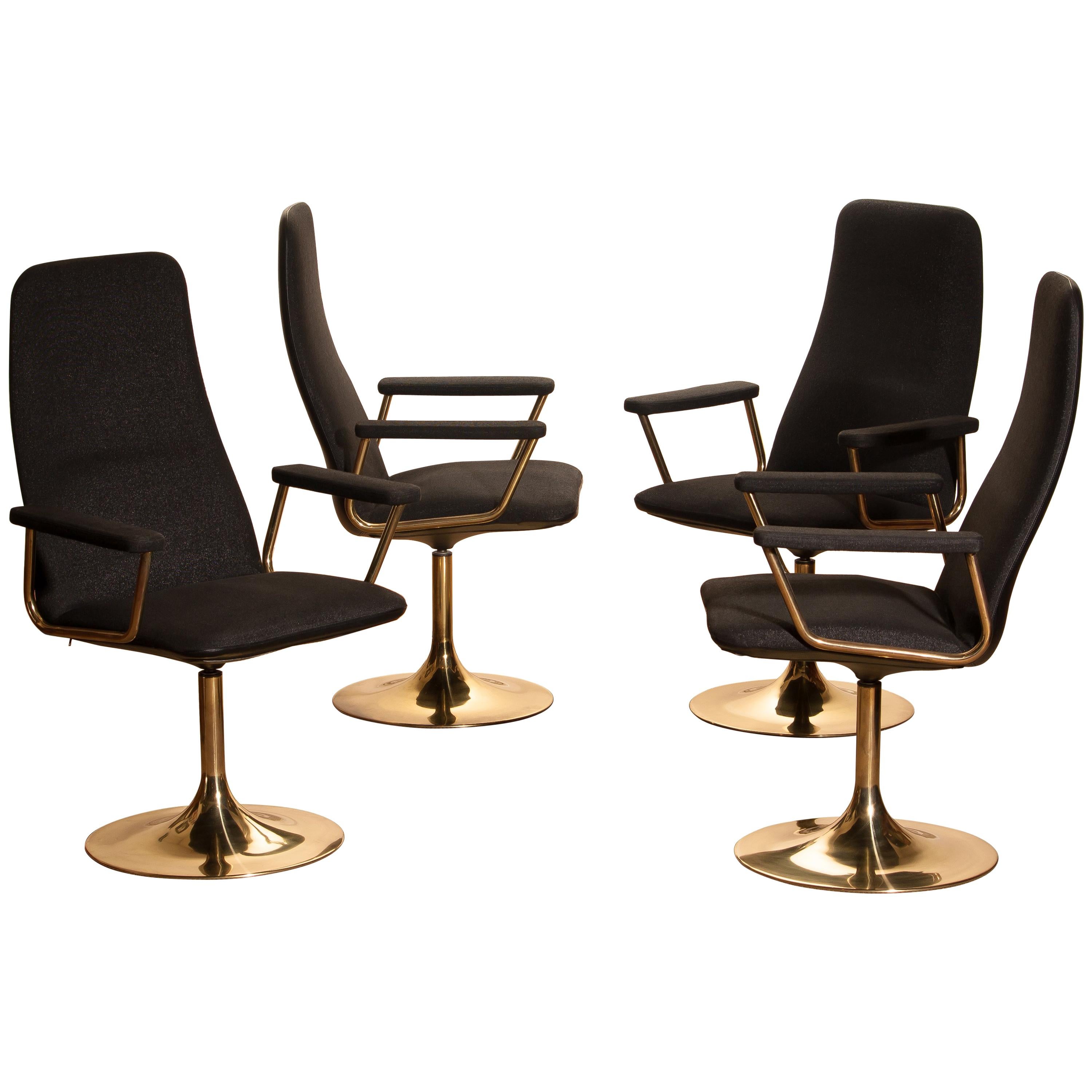 Set of four early production golden swivel chairs with armrests by Börje Johanson Design for Markaryd, Sweden. 
Upholstered with black fabric and black faux leather back on golden steel bases.
The chairs are in a good condition and from the