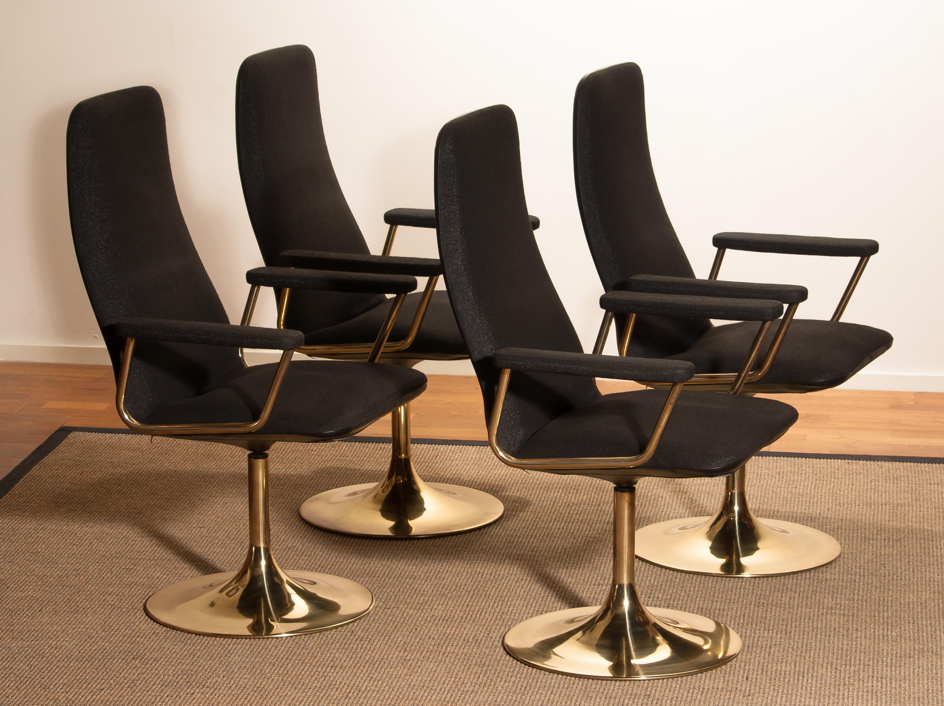 Set of four early production golden swivel chairs with armrests by Börje Johanson Design for Markaryd, Sweden. 
Upholstered with black fabric and black faux leather back on golden steel bases.
The chairs are in a good condition and from the