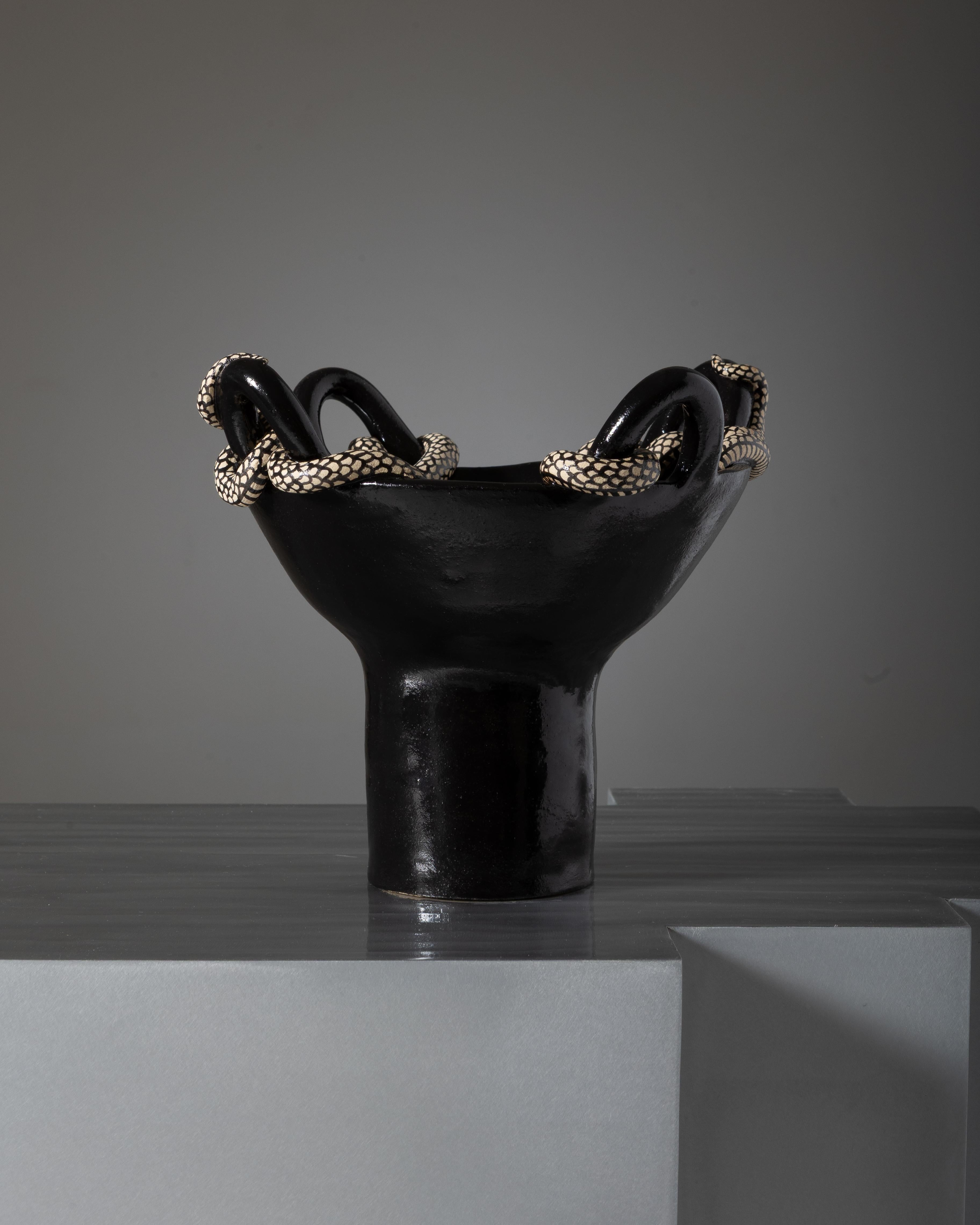 Cuenco con pie y cuatro asas de gres blanco esmaltado en negro, obra de la artista Lohana Saby. Adornado con dos serpientes blancas que se enroscan graciosamente alrededor de las asas.
DV2714