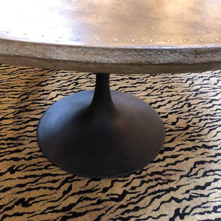 A Powell dining table from four hands. The mixed materials make the table interesting. It features the classic tulip shape but pedestal is a blackened steel. The dining surface is a patchwork of riveted brass that is banded in distressed oak. Small