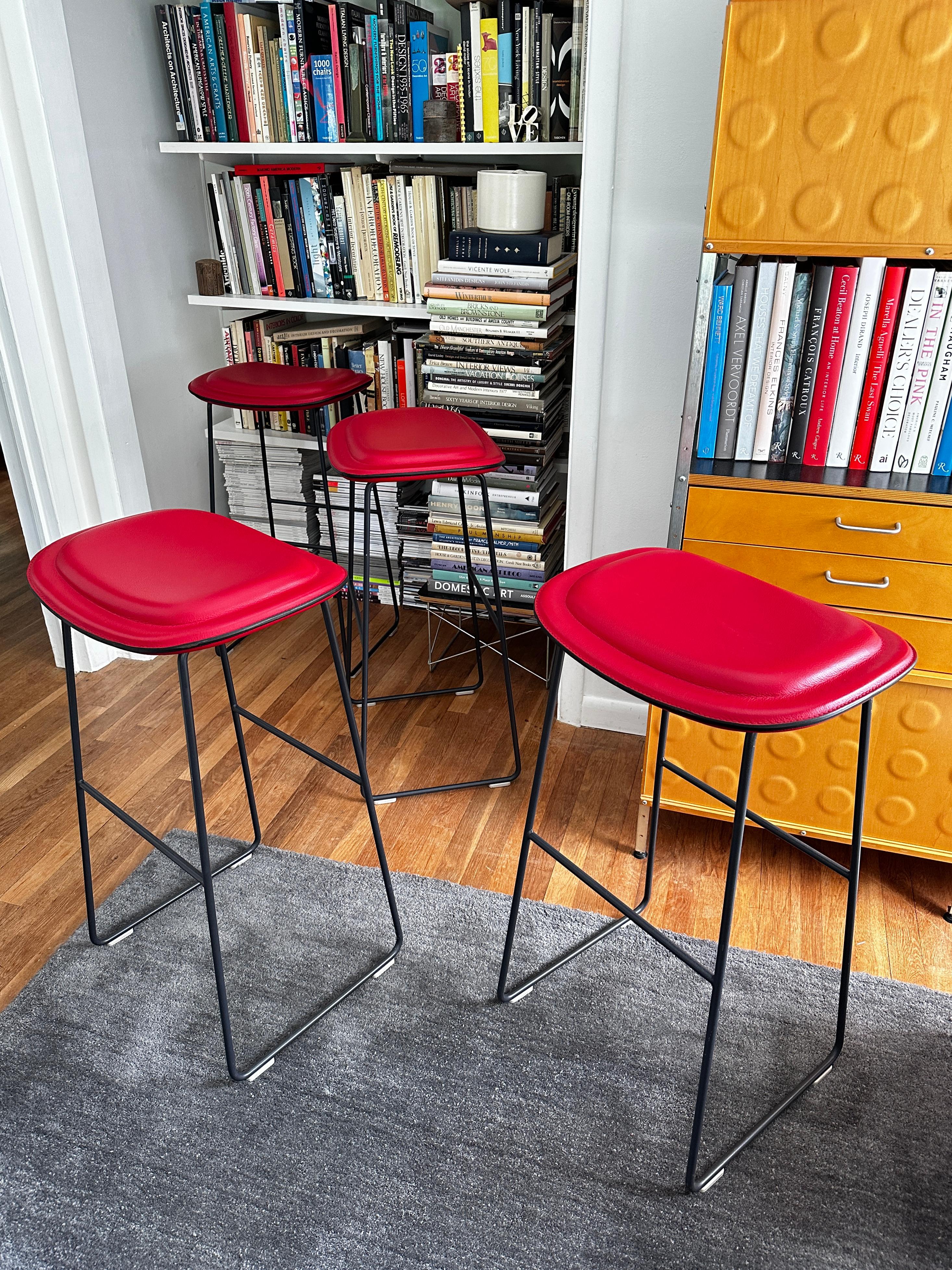 Vier Hi Pad Hocker, entworfen von Jasper Morrison im Jahr 2003 für Cappellini.  Die Sitze sind mit rotem Leder bezogen und haben ein Gestell aus grau lackiertem Edelstahl, das auf vier Polypropylen-Gleitern ruht.  Von den drei verfügbaren Größen