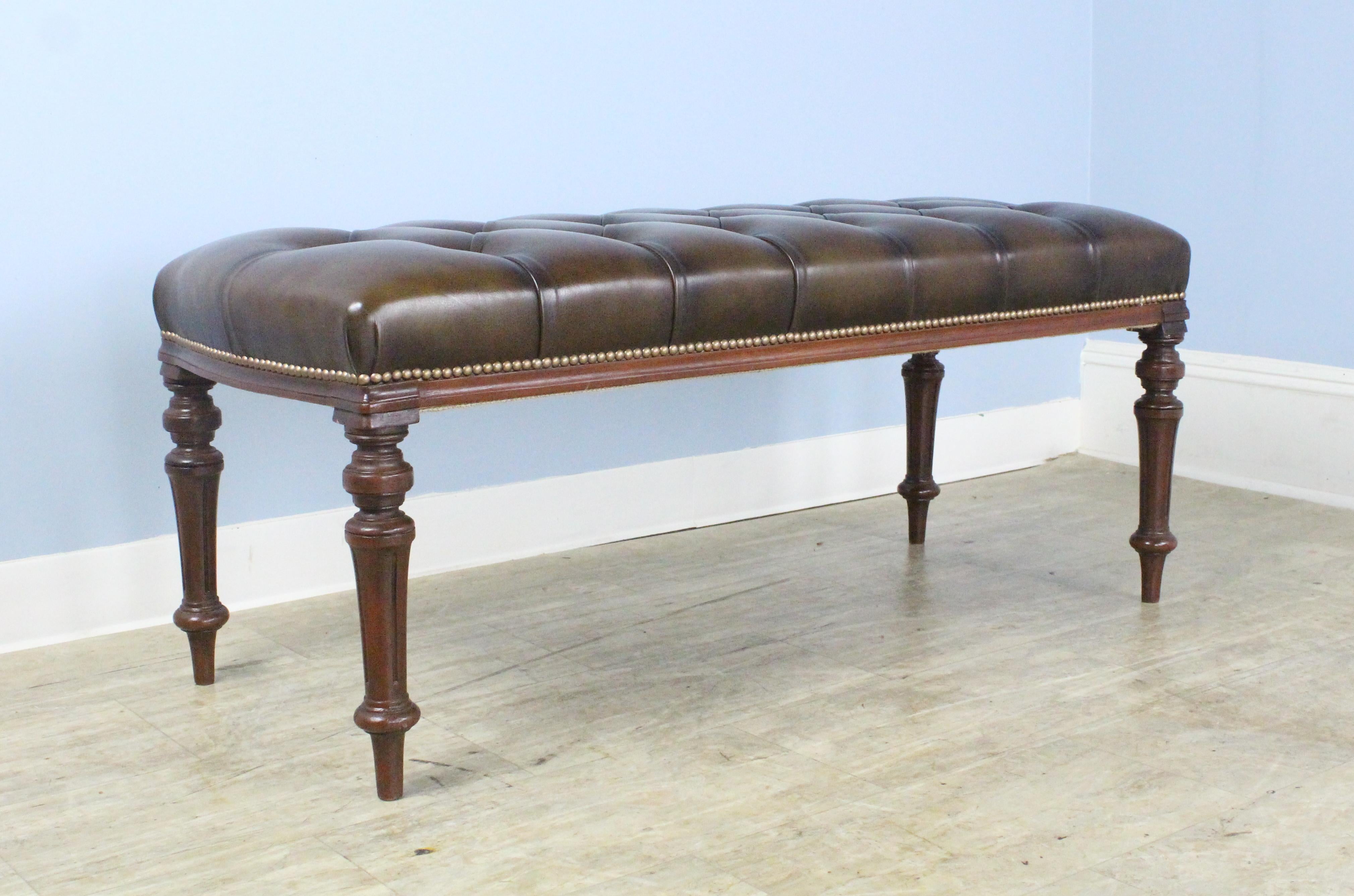 A handsome mahogany bench with turned legs, newly upholstered in tufted brown leather. The leather is in sparkling condition, with decorative rivets at the legs. Height is good for seating or as a coffee table, with or without a tray on top.