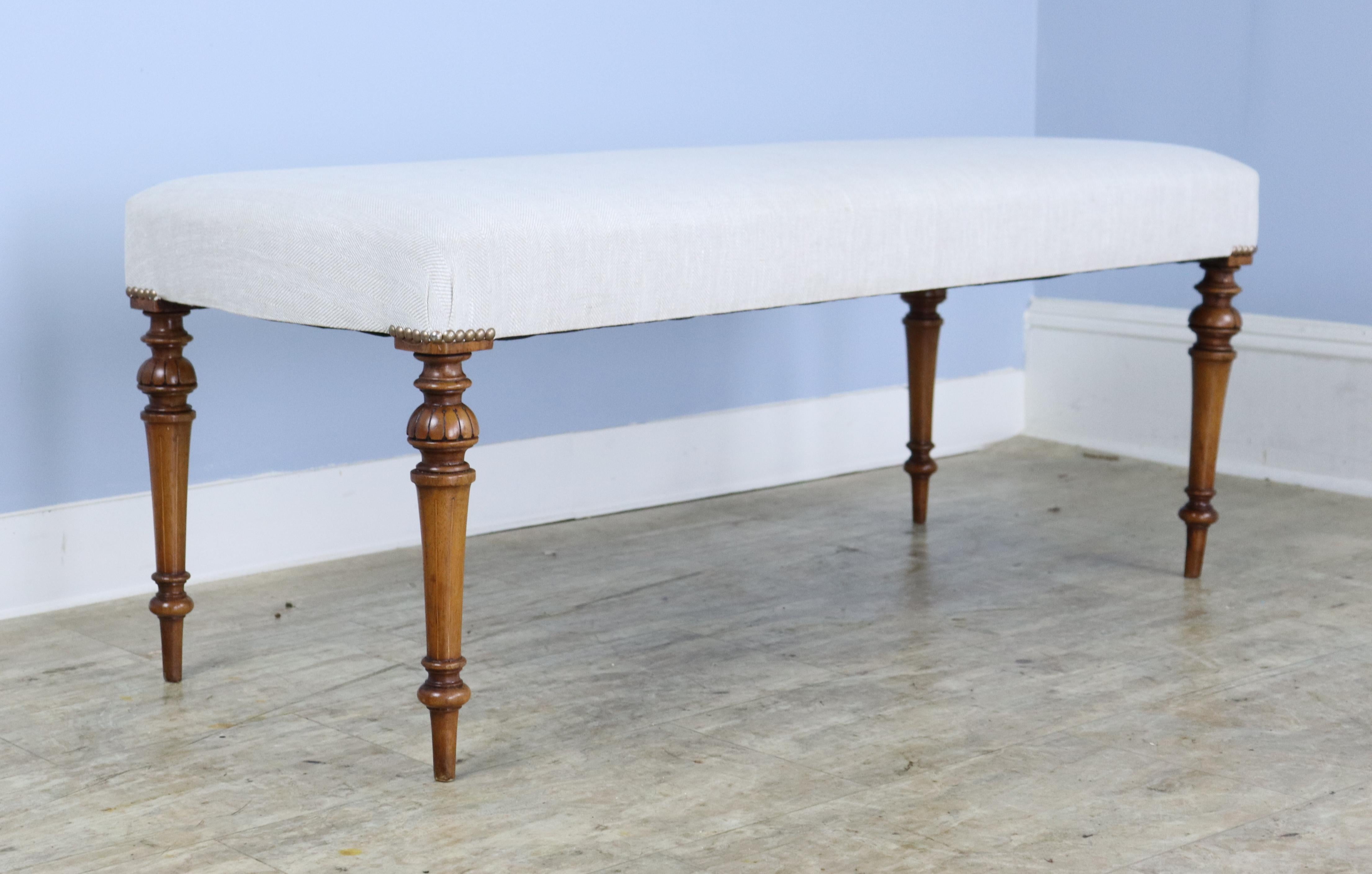 An elegant stool newly covered in French beige linen, with decorative nailheads at the corners of the seat. Constructed with mahogany legs, intricately carved and inlayed with what we believe is satinwood.  Very good sitting-height, comfortable