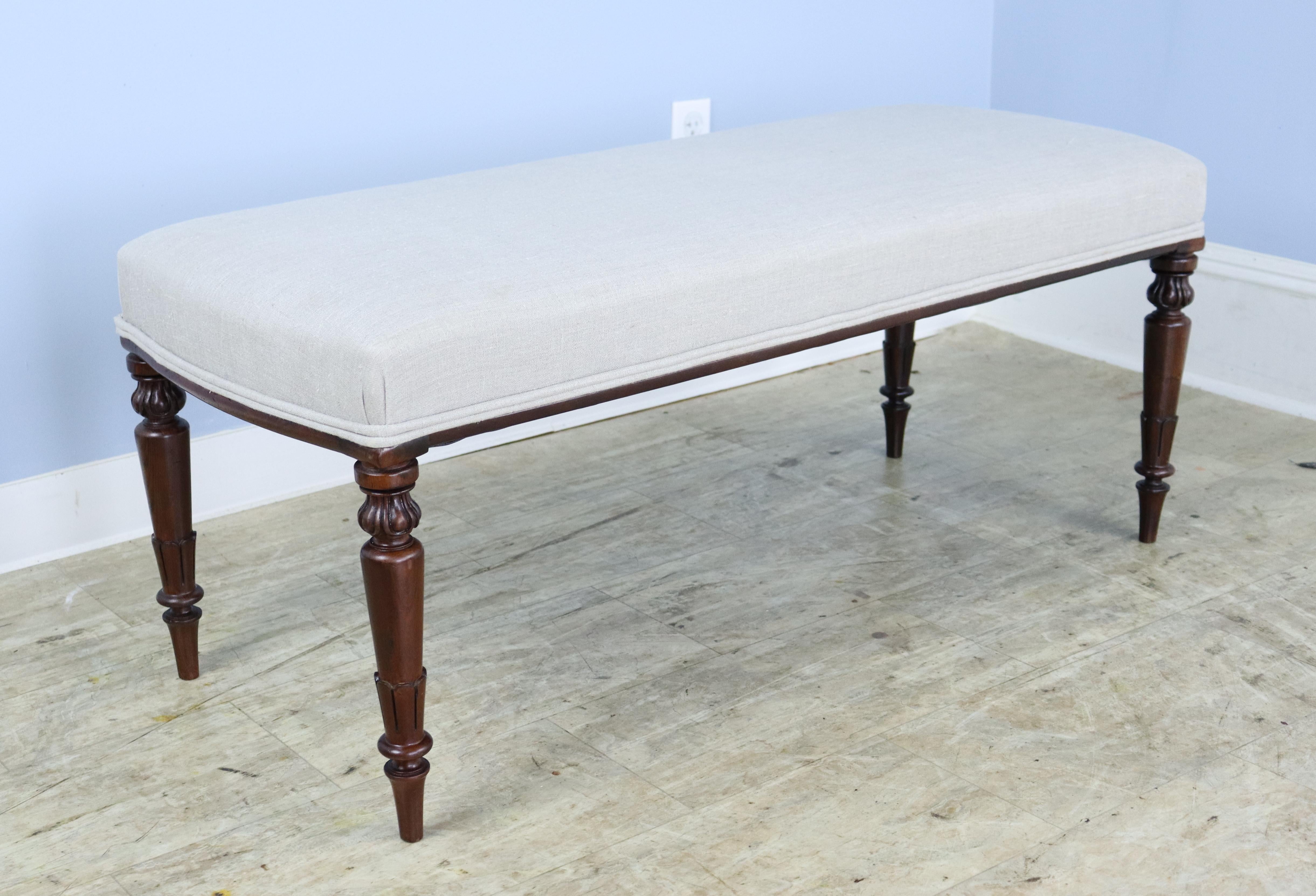 An elegant stool newly covered in French beige linen, with decorative piping at the edge of the seat. Constructed with mahogany legs, circa 1890 that are well-carved and sturdy. Very good sitting-height, comfortable seating at the end of the bed.