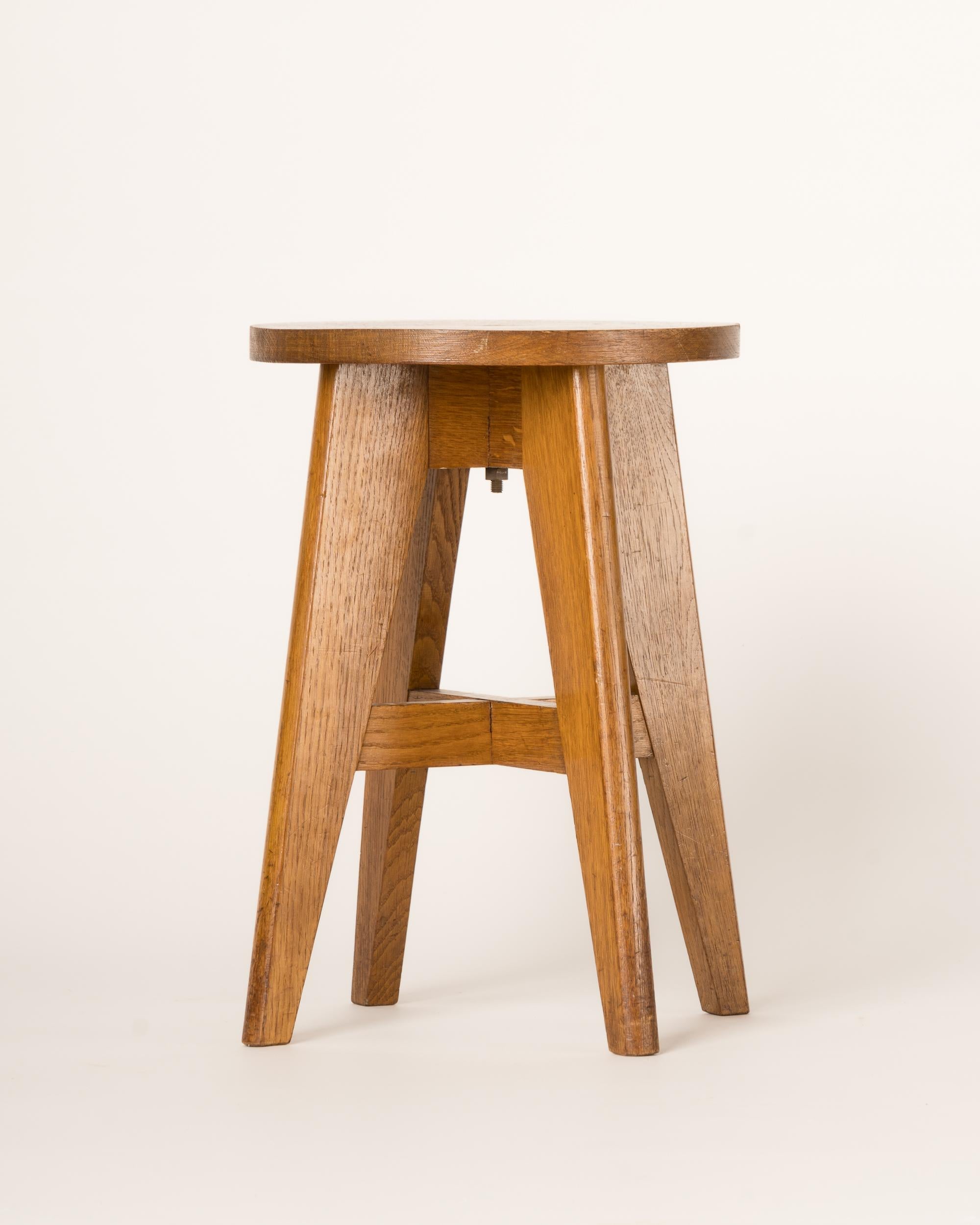 A minimalist solid oak four legged stool with a brass screw on top. In the style of Pierre Jeanneret. A second identical stool is available but currently upholstered with a leatherette top (needs to be re-upholstered). 
Sturdy. Some stains on top.