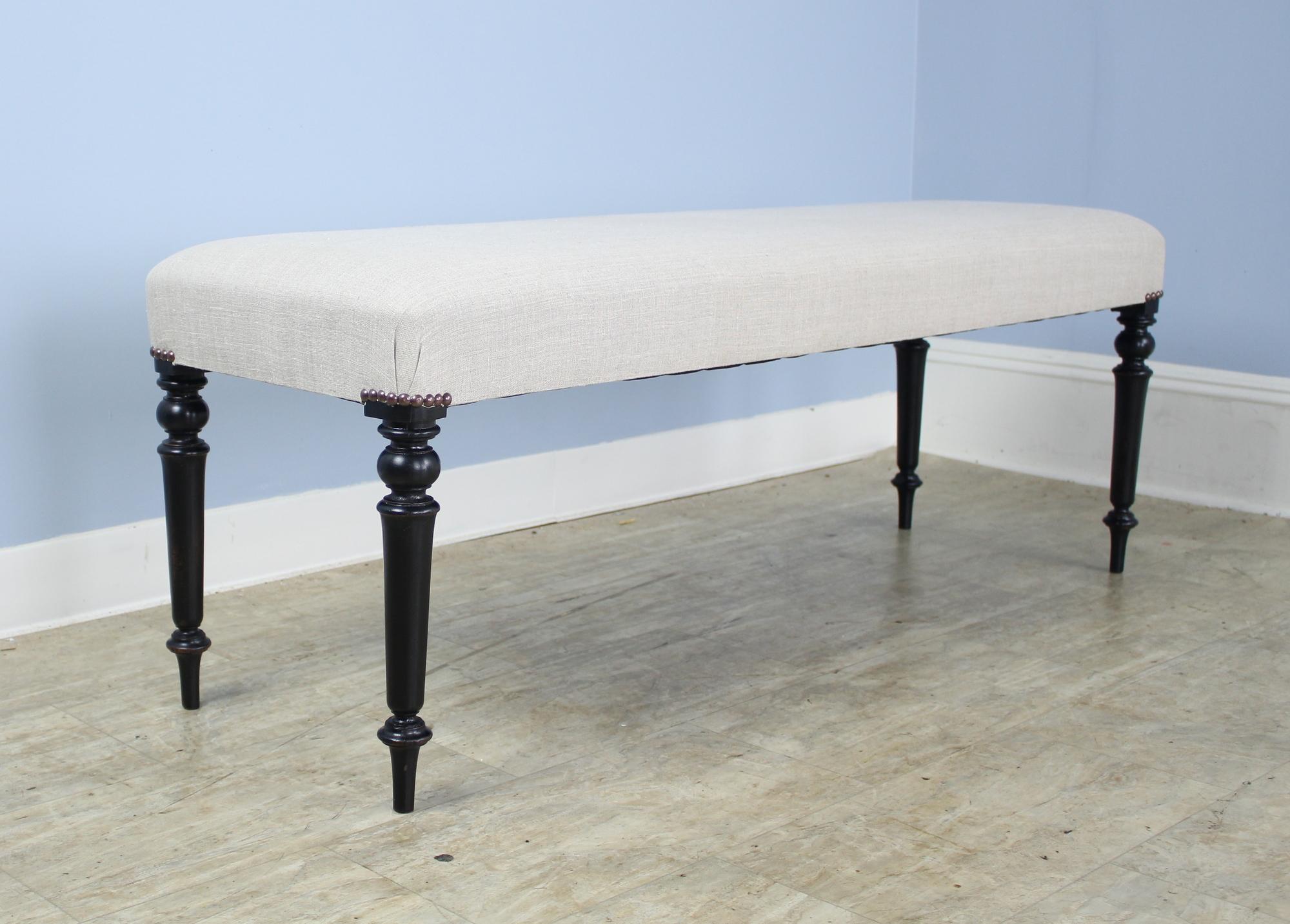 An elegant stool newly covered in French beige linen, with brass decorative upholstery nails. Graceful and well shaped upholstered corners. Sturdy construction and well turned ebonized legs. Very good sitting-height, comfortable seating at the end