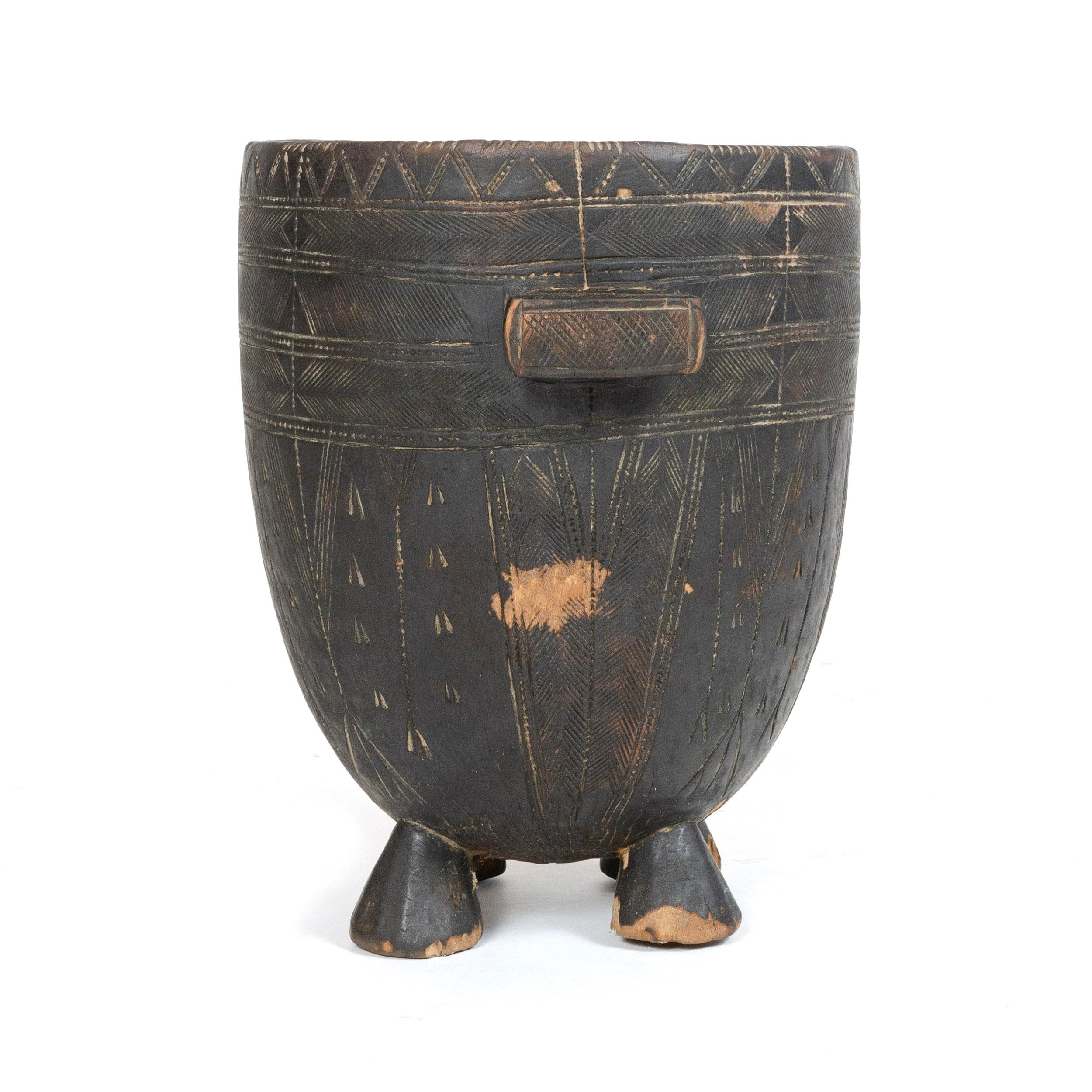 A robust vessel with a single handle on four legs, carved from one continuous piece of wood.