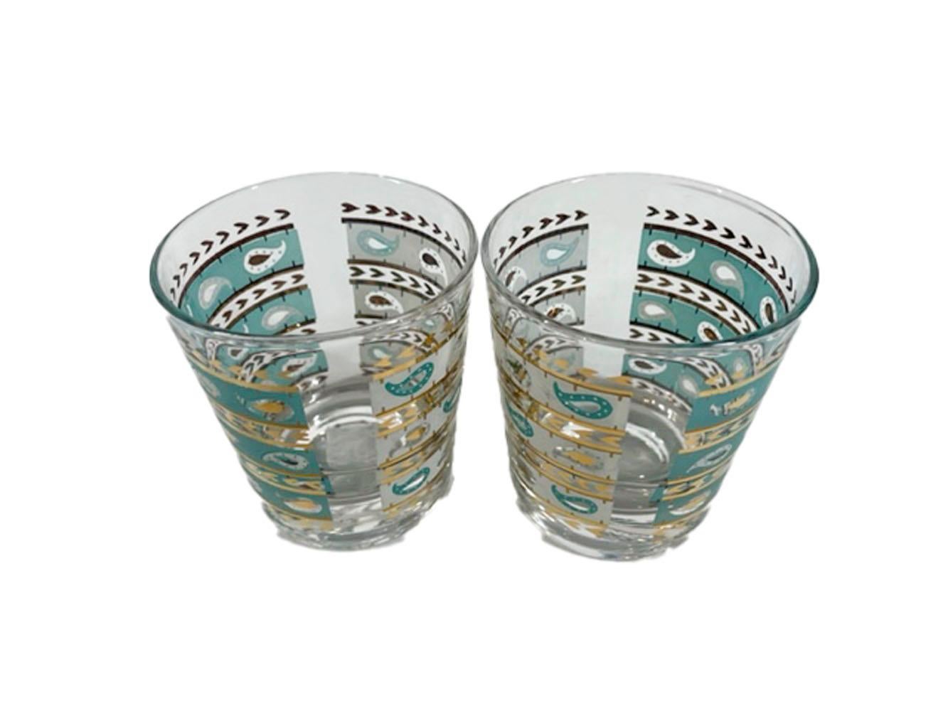 Four Mid-Century Modern old-fashioned glasses designed and decorated by Gay Fad. Each glass is decorated on one side in aqua and the other in white with alternating bands of gold as well as the colored bands having paisley elements in the other