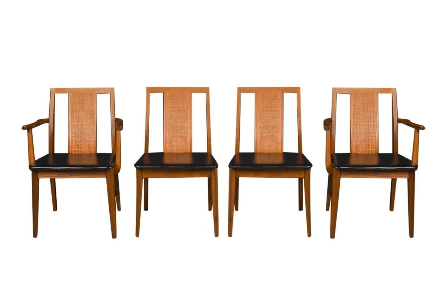 A beautiful set of four mid century modern chairs two arm chairs and two side chairs, in the style of Edward Wormley. This set features solid walnut frames with black faux leather seats. A classic minimalistic design with a sleek angled backrest