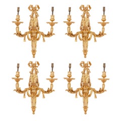 Quattro applique a due luci in stile neoclassico in bronzo dorato