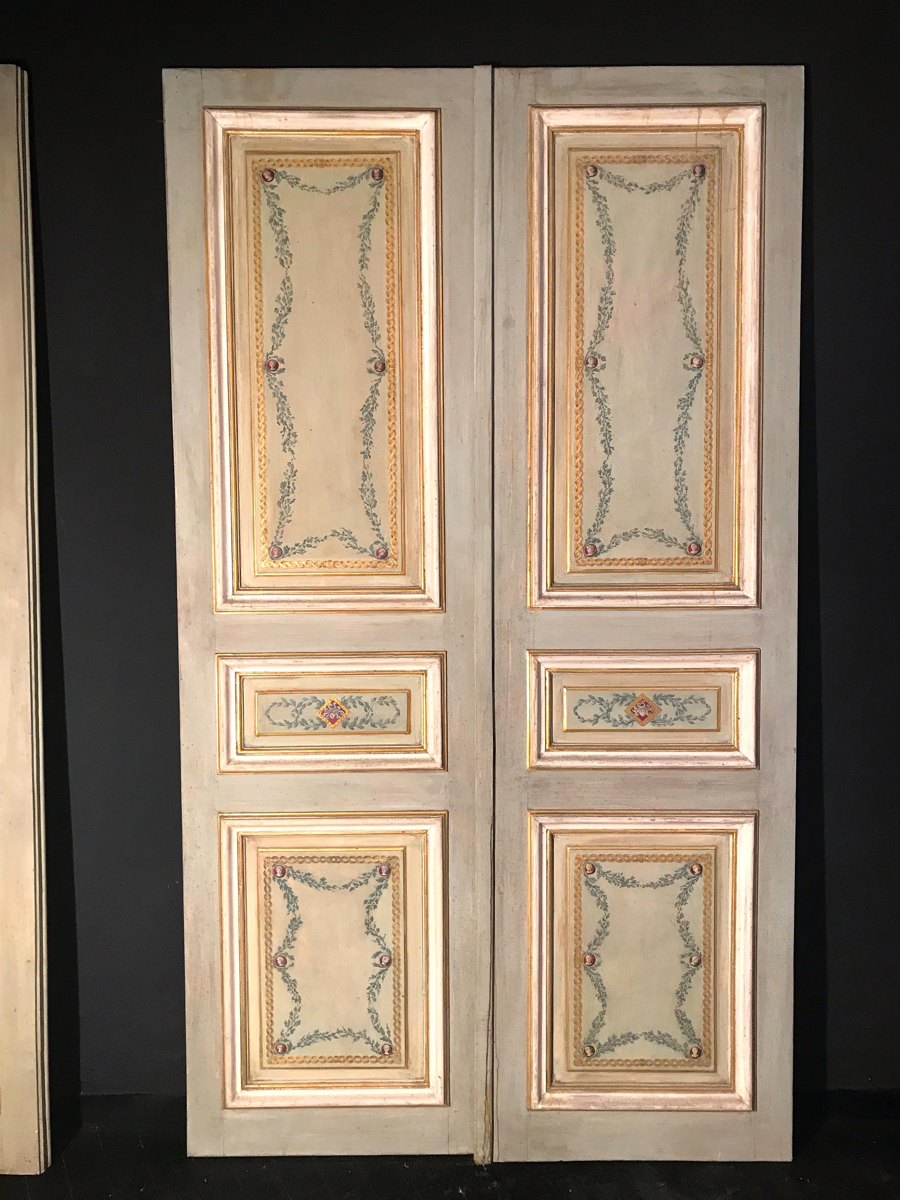 Elegant Italian finely paneled wooden doors, decoratively painted, from the mid-19th century. The doors feature a single front recessed panel painted with foliage and geometric designs in various shades of gray, light blue and ivory color centered