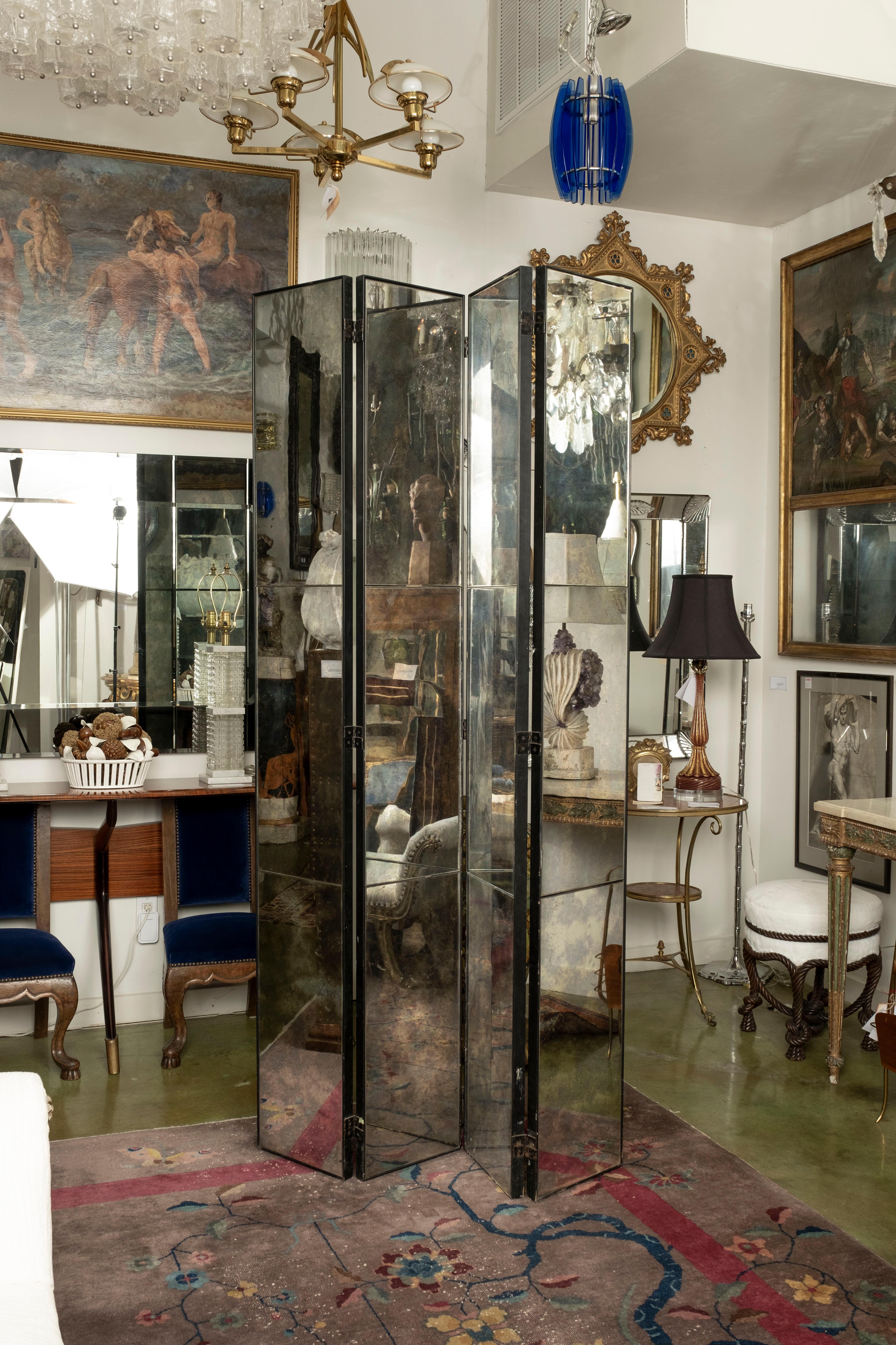 Four panel antiqued mirrored room divider screen. This glamorous Hollywood Regency Maison Jansen style antiqued mirror screen set in an iron frame is comprised of four 12 inch panels with three sections of mirror on each. Our versatile screen can be