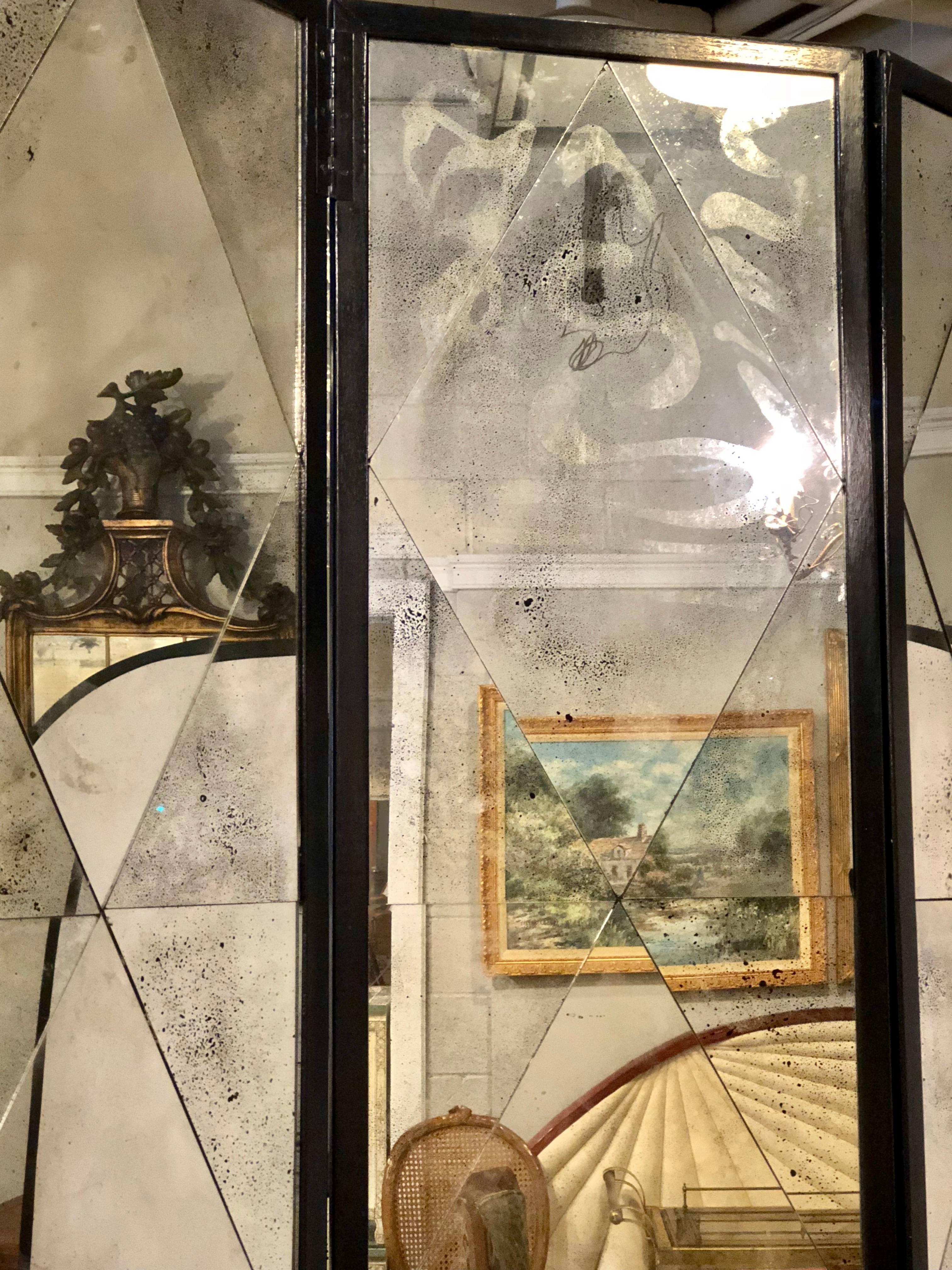 A Hollywood Regency style four panel double sided floor screen or room divider having a distressed diamond mirror design. There is a break/long scratch on one of the mirrored panels and a couple of the panels have been replaced as is evident in the