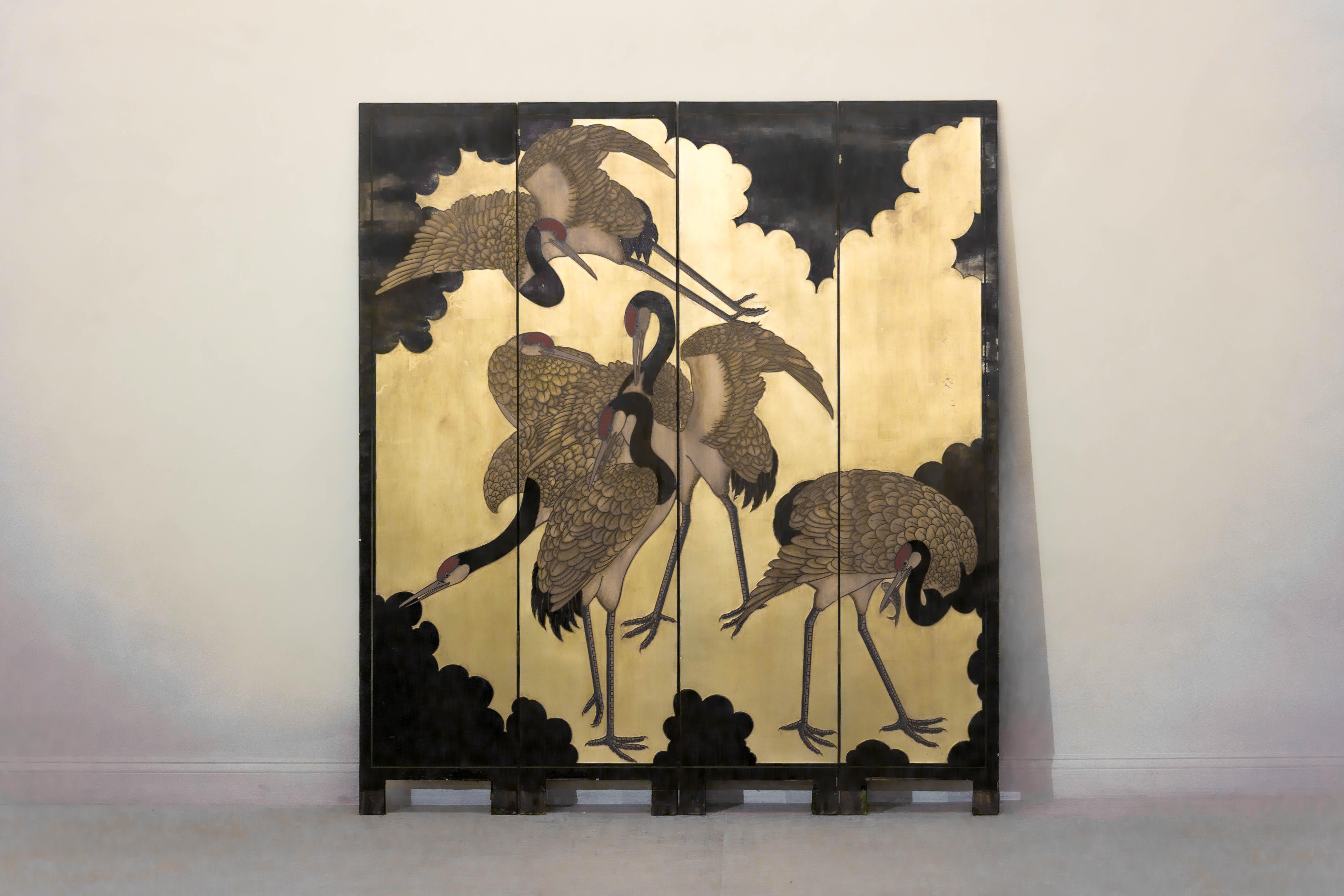 Dieser vierteilige Paravent zeigt ein dramatisches Vogeltableau im japanischen Stil, das sowohl durch seine Größe als auch durch seine Ausführung besticht. Vor einem vergoldeten Hintergrund, der mit stilisierten schwarzen Wolkenformen bepinselt ist,
