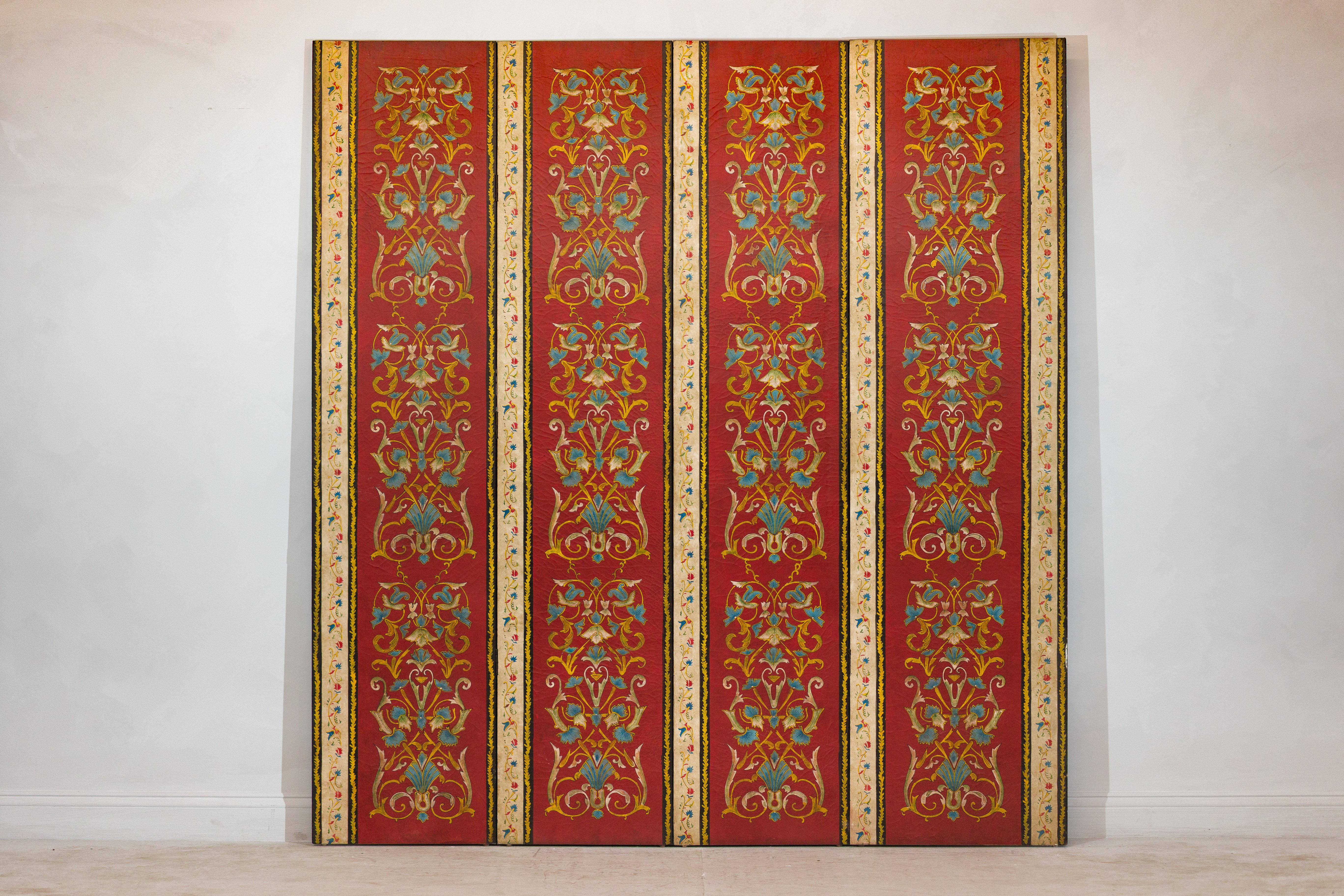 This vintage four-panel screen features a striking crimson red ground embellished with intricate hand-painted scrollwork in a classical floral motif. Each panel is framed by vertical cream-toned borders adorned with delicate vines and stylized