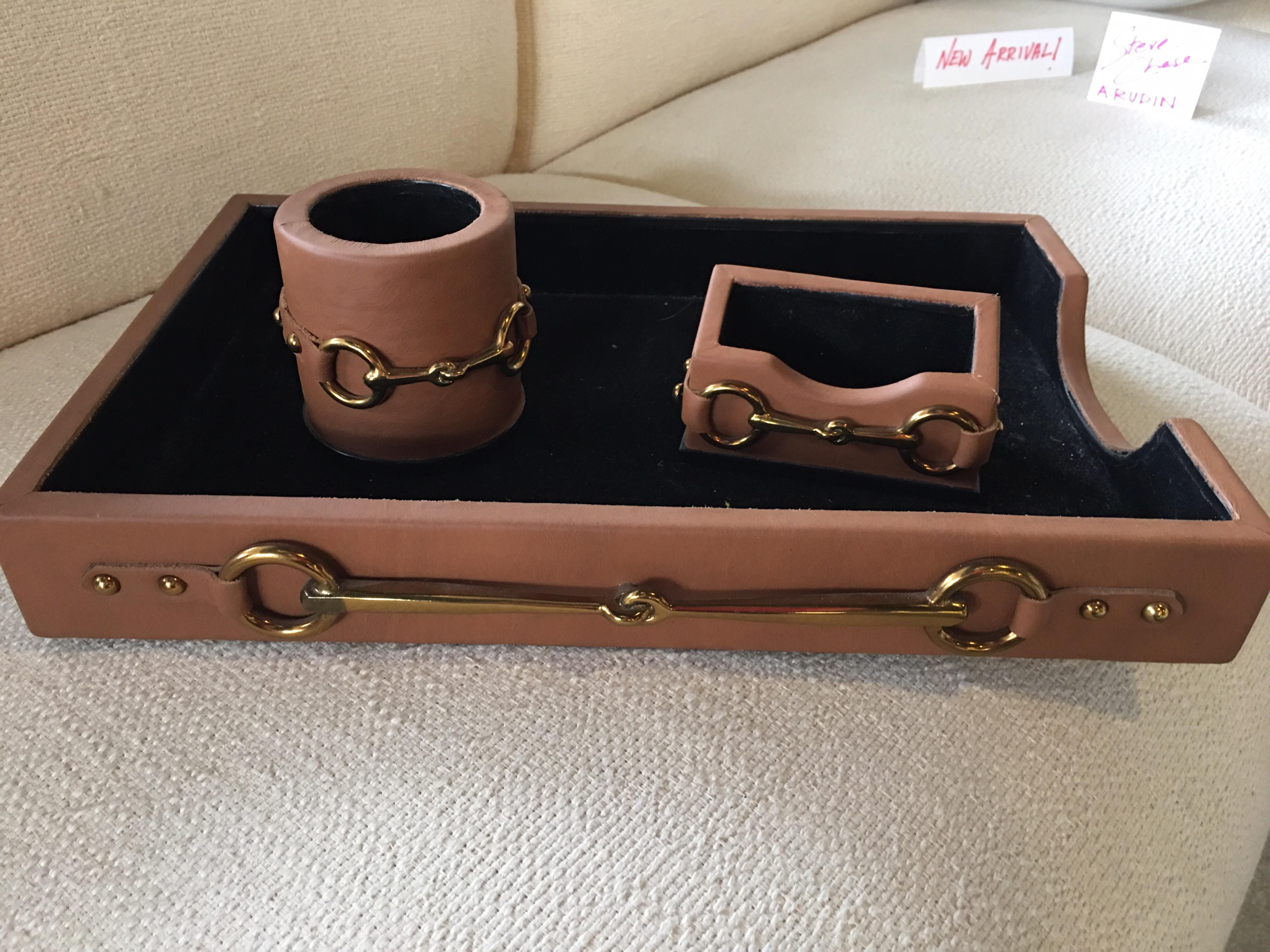 A gorgeous four piece desk set in leather and brass detail by Maitland Smith hand made in the Philippines. Very much in the style of Gucci with brass horse bits. Never used. From a chic Palm Springs Estate. Letter tray, covered box, pencil holder