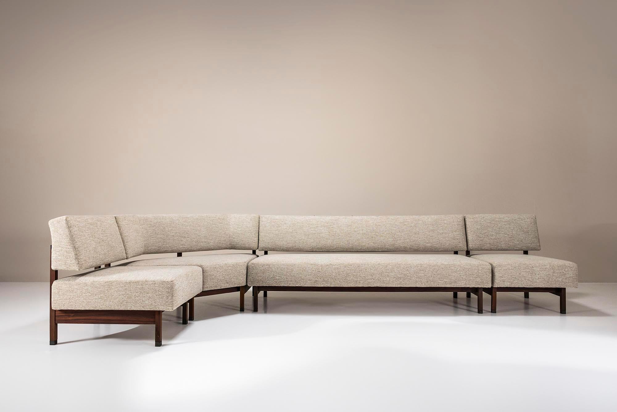 This living room set, veneered in rosewood and newly reupholstered in an off-white fabric, presents a harmonious balance of clean lines and understated elegance. Comprising two lounge chairs, a sofa, and a corner piece, it offers flexibility and