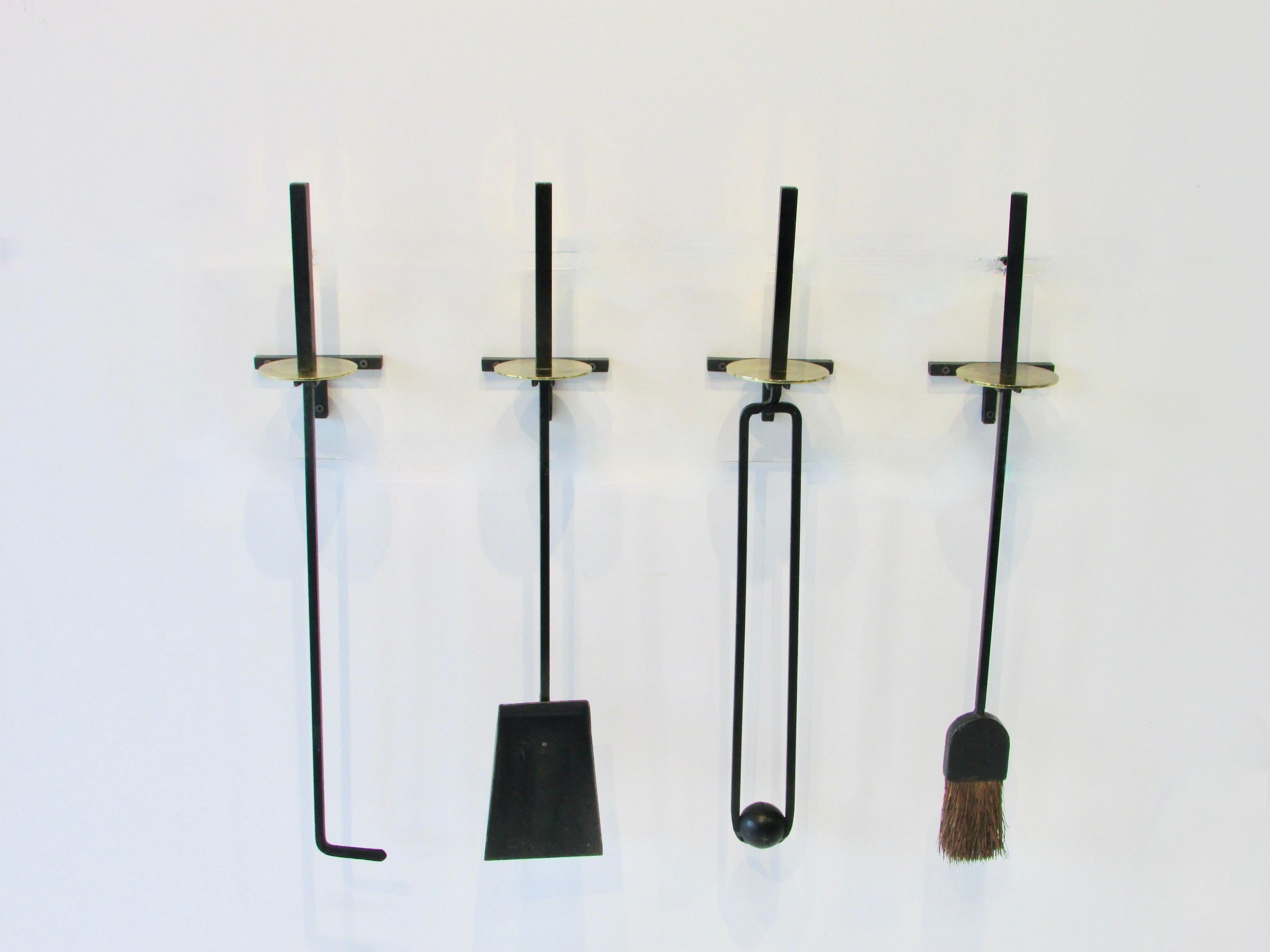 Rare four piece set of Mel Bogart wall mounted fire place tools. Square stock wrought iron tools with brass disc accent. Tools mount into individual wall mount wrought iron holders.