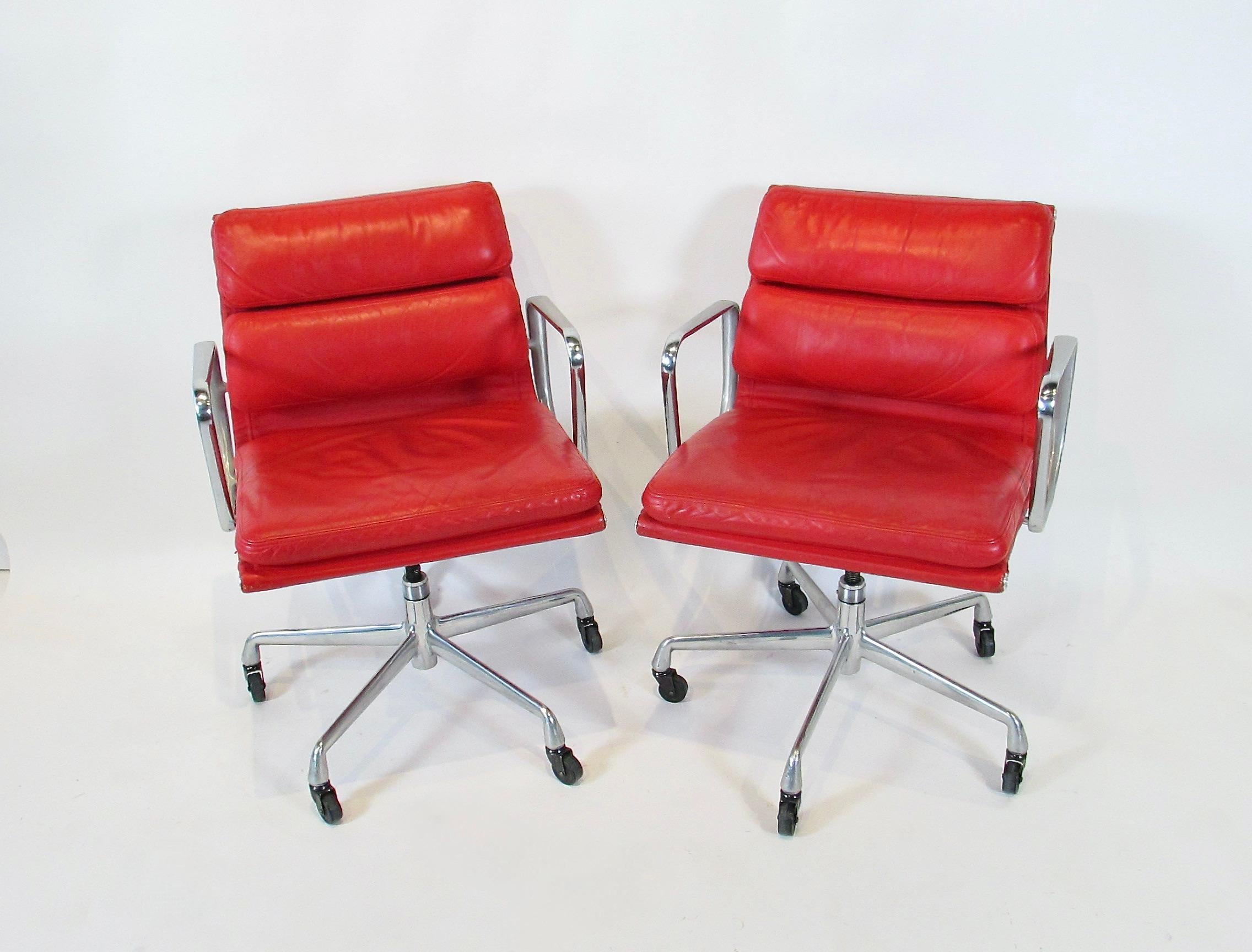 Attraente set di quattro sedie direzionali Eames in alluminio con pad morbido. Set raffinato in pelle rossa originale che non è più disponibile. Gli angoli superiori del retro presentano segni di sfregamento e sono stati ritoccati (come mostrato). 