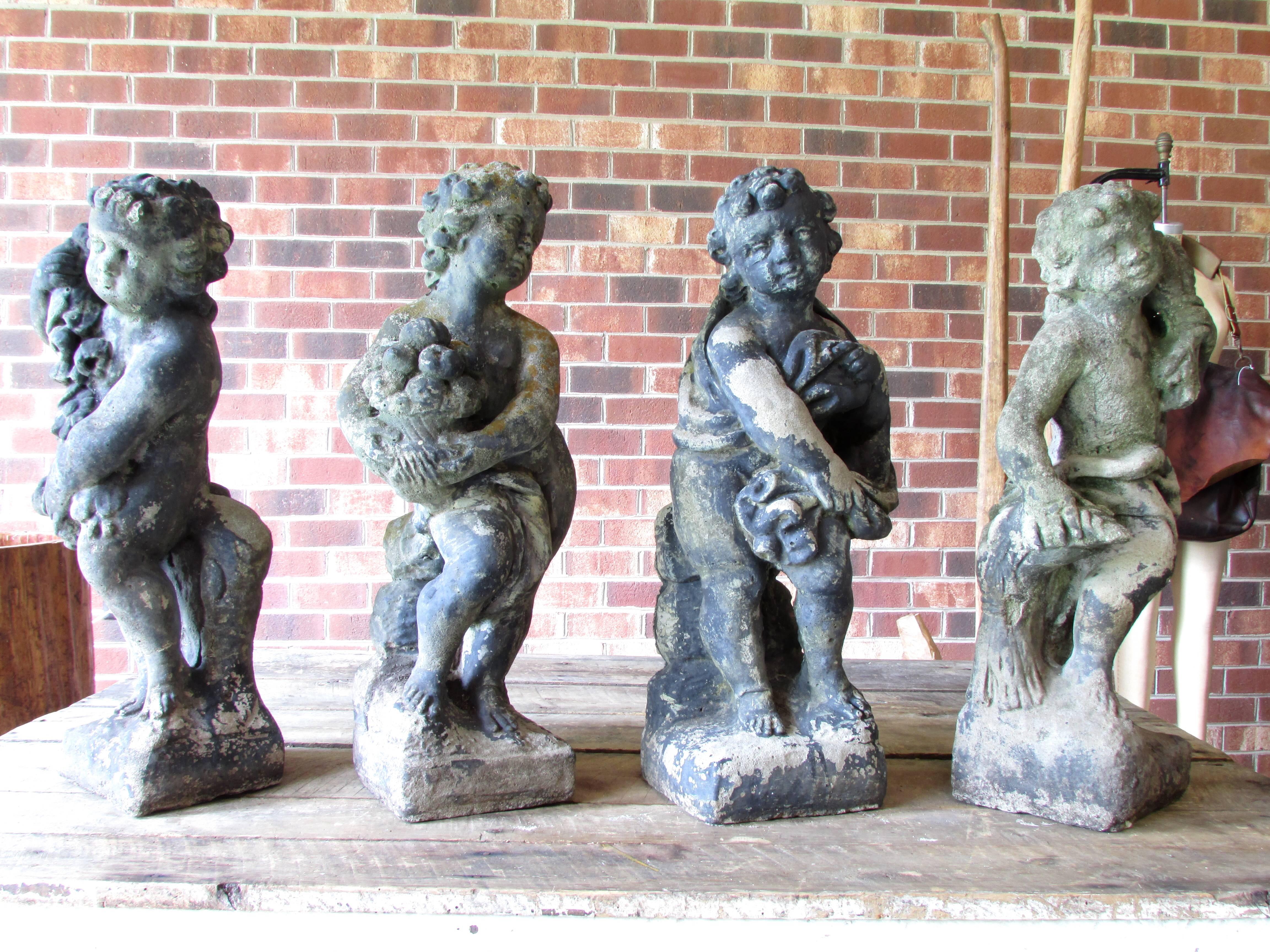 Set of four cast stone cherub statues depicting the four seasons based on Greek classical mythology the cherub with cloth and crossed arms to signify the cold temperature winter, cherub with fresh picked flowers depicting spring, cherub with basket